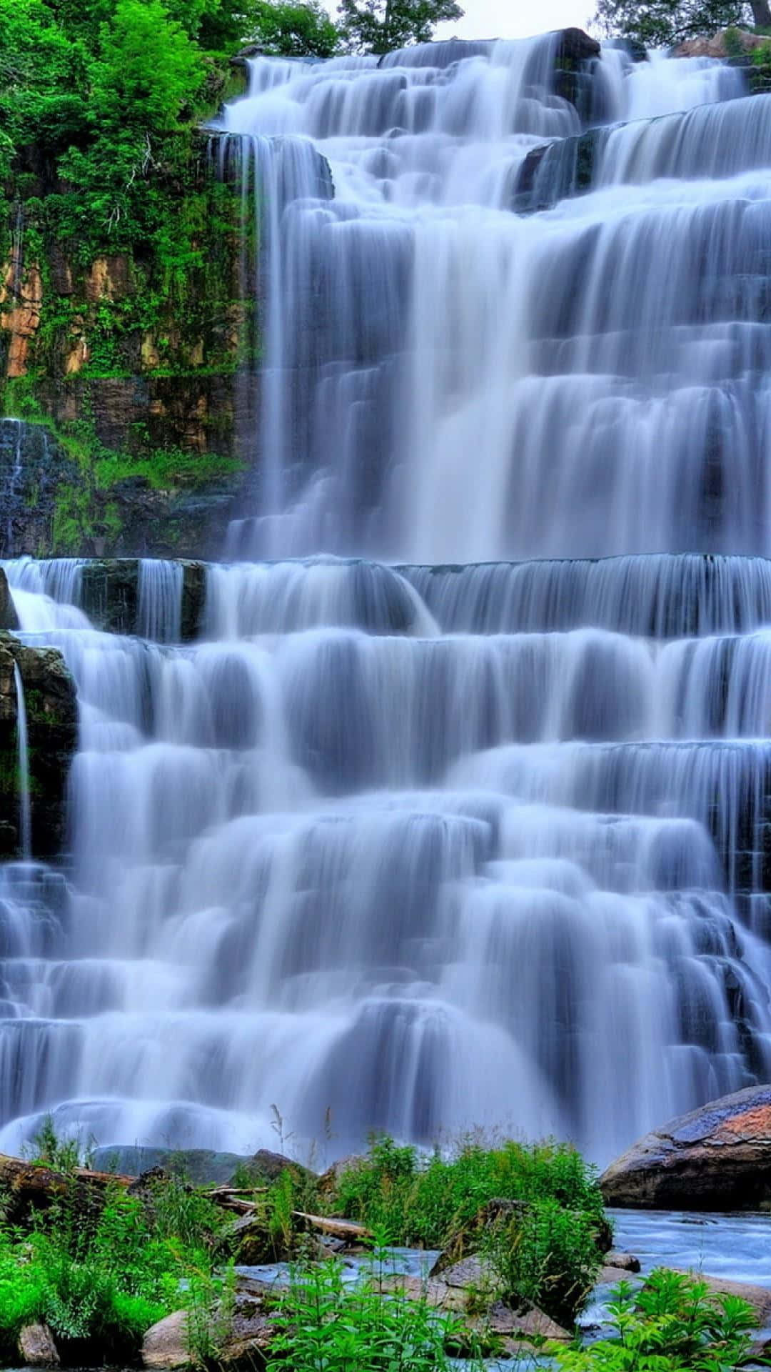 Waterfalls 桌布 壁紙 — 一座雄偉的多層瀑布穿過茂密的綠色森林，伴隨著霧氣和岩石壁架。