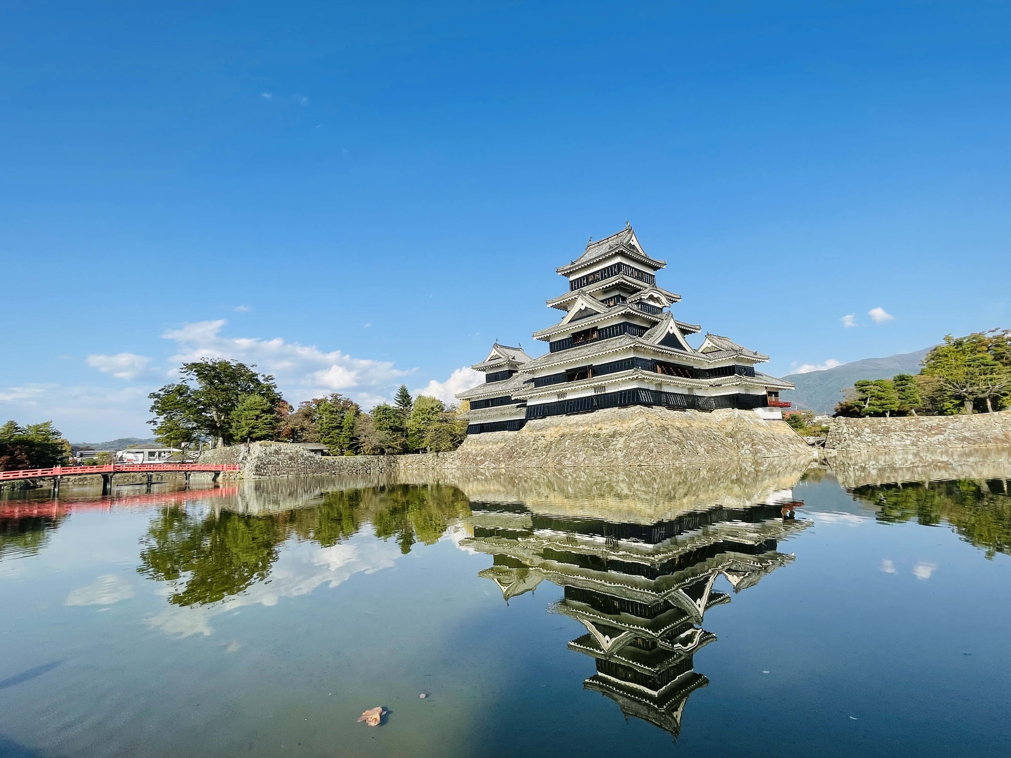 水 桌布 壁紙 — 一座雄偉的日本城堡，層疊的屋頂在清澈藍天下完美倒映在平靜的水面上。