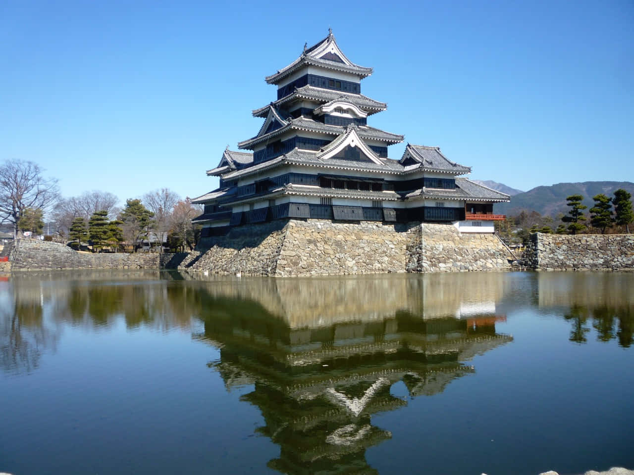 日本 桌布 壁紙 — 一座雄偉的日本城堡，層疊的屋頂在平靜的水面上完美倒映，天空清澈湛藍。