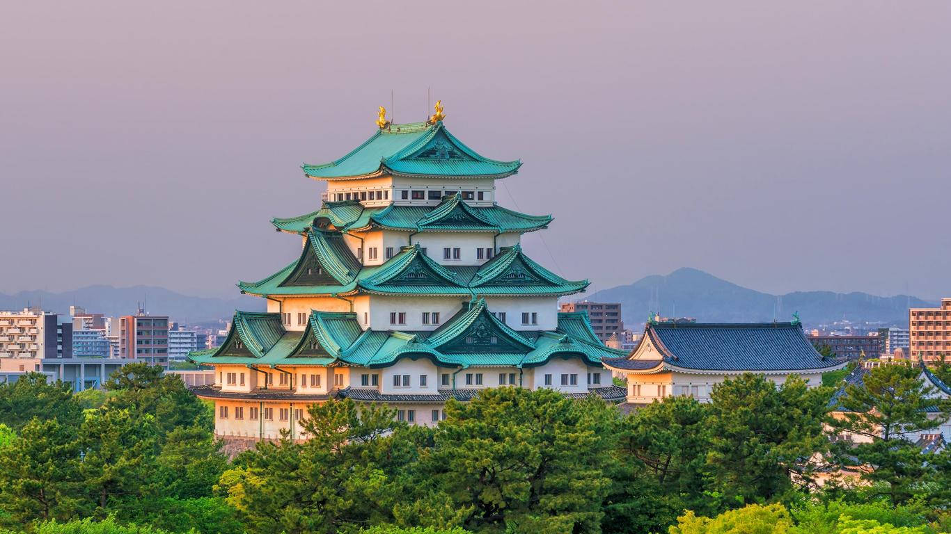 Nagoya 桌布 壁紙 — 一座雄偉的日本城堡，擁有綠色瓦片屋頂，在柔和的紫色暮色天空中，聳立在茂密的樹木之上。