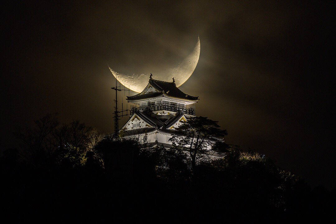 Himeji Castle 桌布 壁紙 — 一座雄偉的日本城堡在夜晚被照亮，一輪發光的彎月完美地框在其傳統屋頂後方。