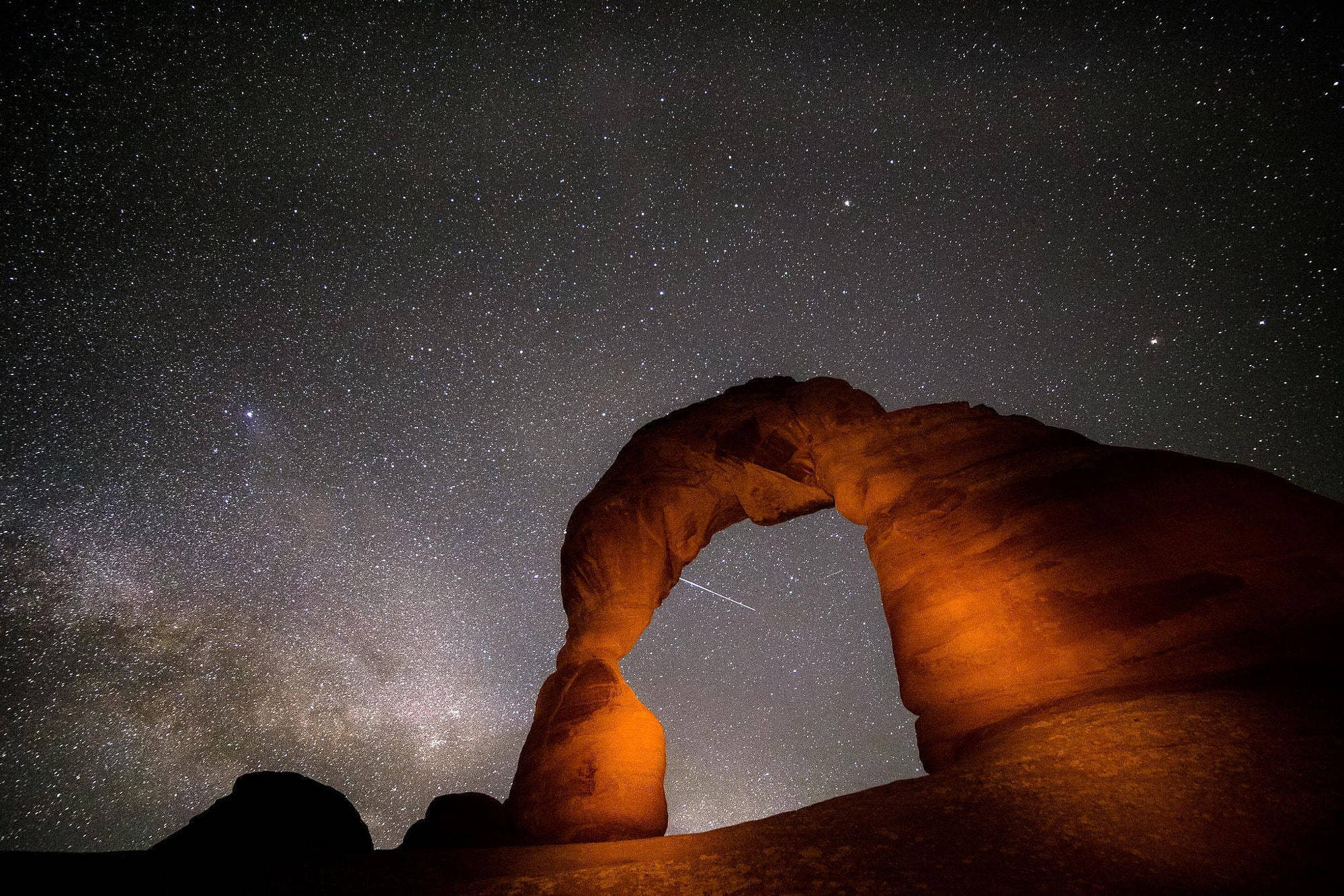 Stars 桌布 壁紙 — 一座雄偉的橙色砂岩拱門在星爆天空下發光，銀河在其上方拱起。