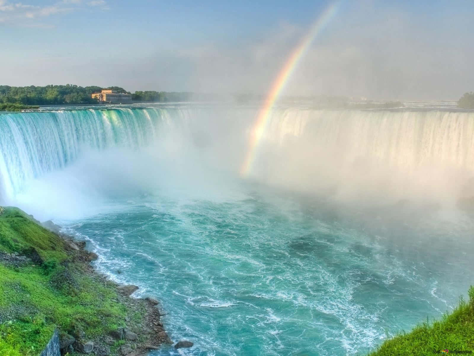 720p Niagara Falls 桌布 壁紙 — 一座雄偉的瀑布傾瀉而下，流入碧綠色的水域，一道鮮豔的彩虹在霧氣中拱起。