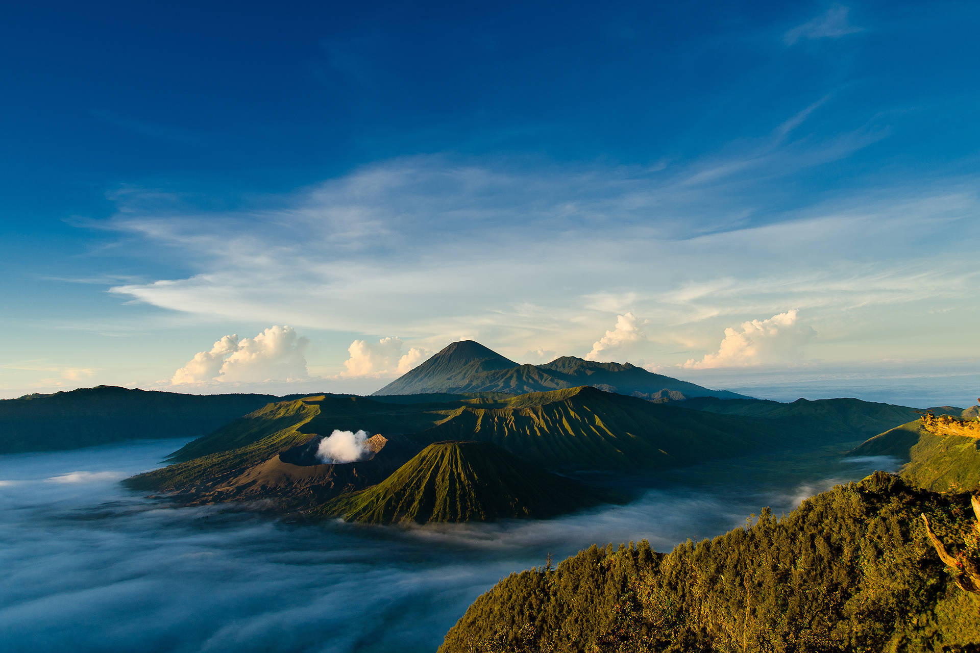 印尼 桌布 壁紙 — 一座雄偉的火山聳立在雲海之上，在蔚藍的天空下，點綴著柔軟的白雲。