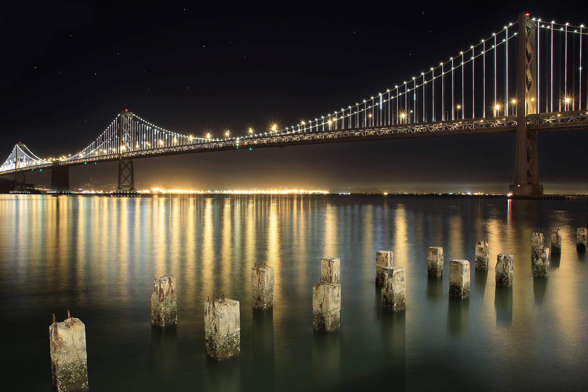 San Francisco 桌布 壁紙 — 一座雄偉的照明吊橋在夜晚橫跨平靜的水道，伴隨著星空和發光的倒影。