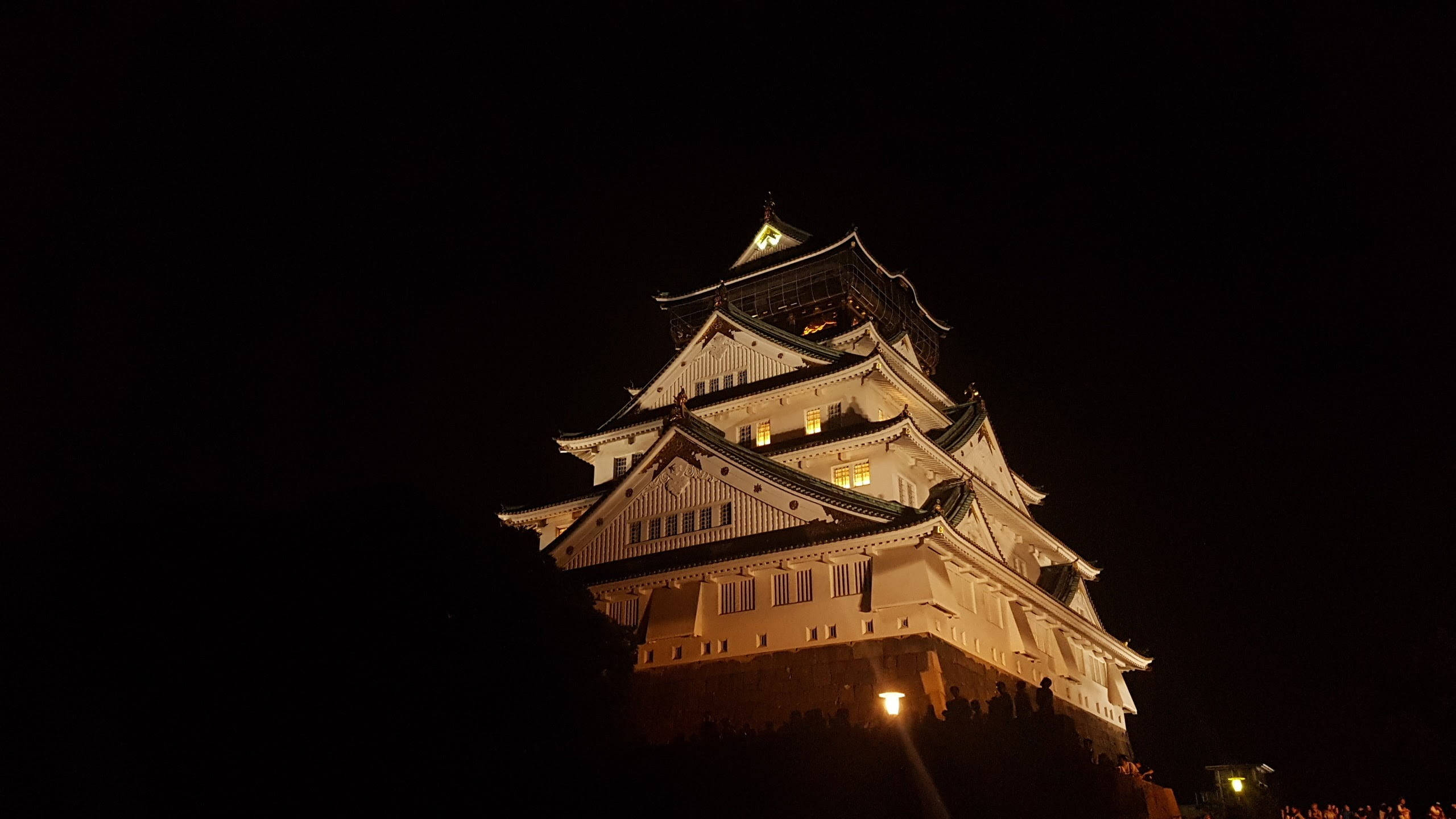 Osaka Castle 桌布 壁紙 — 一座雄偉的燈光照明日本城堡聳立在漆黑的夜空下，窗戶透出溫暖的光芒。