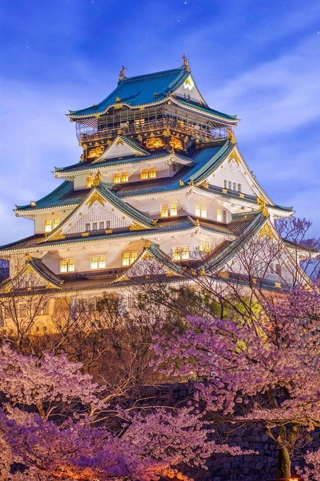 Himeji Castle 桌布 壁紙 — 一座雄偉的燈光璀璨的日本城堡，在暮色天空下聳立於盛開的粉紅櫻花之上。