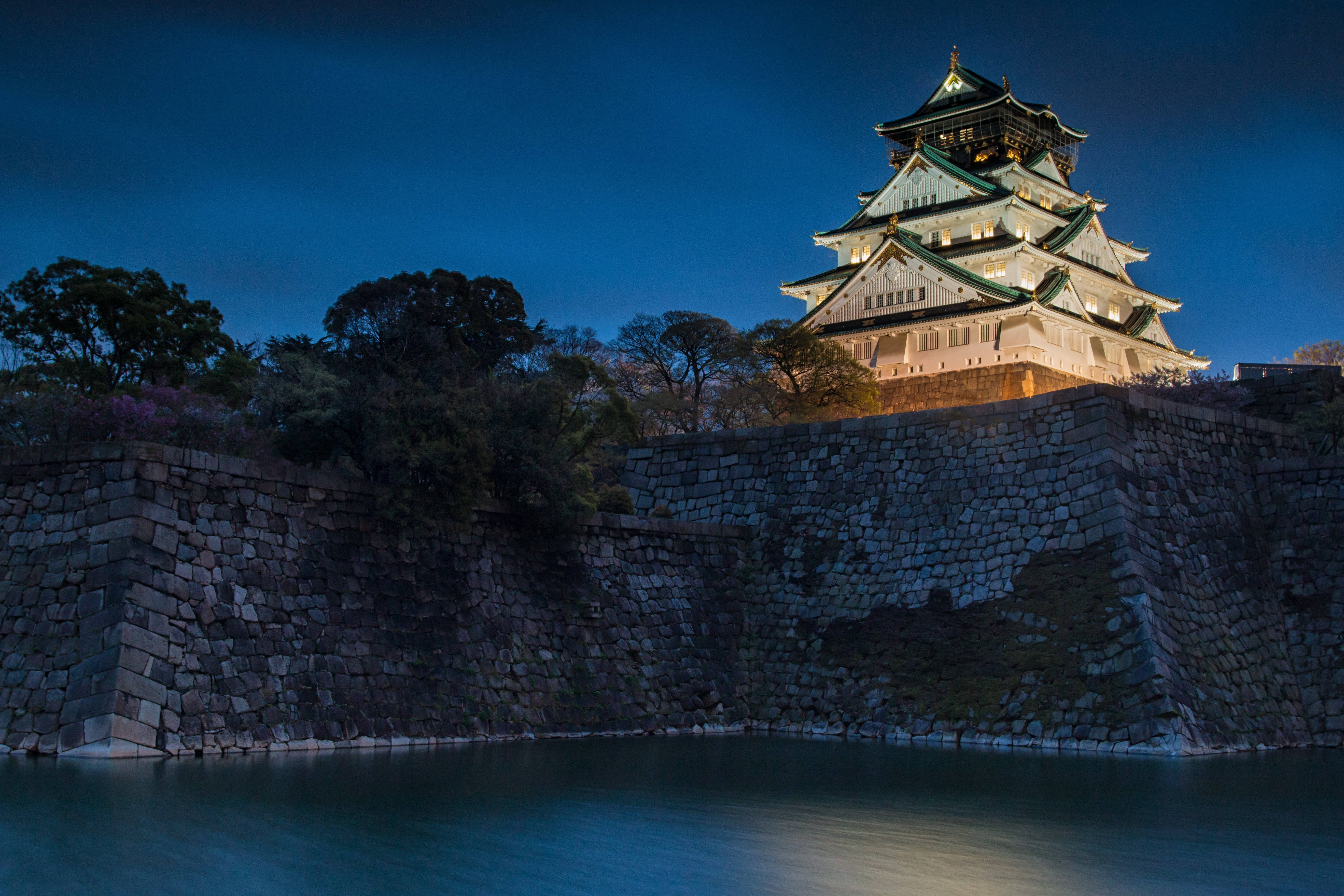 Osaka Castle 桌布 壁紙 — 一座雄偉的燈光璀璨的日本城堡在深藍色的暮色天空下矗立在平靜的護城河上。