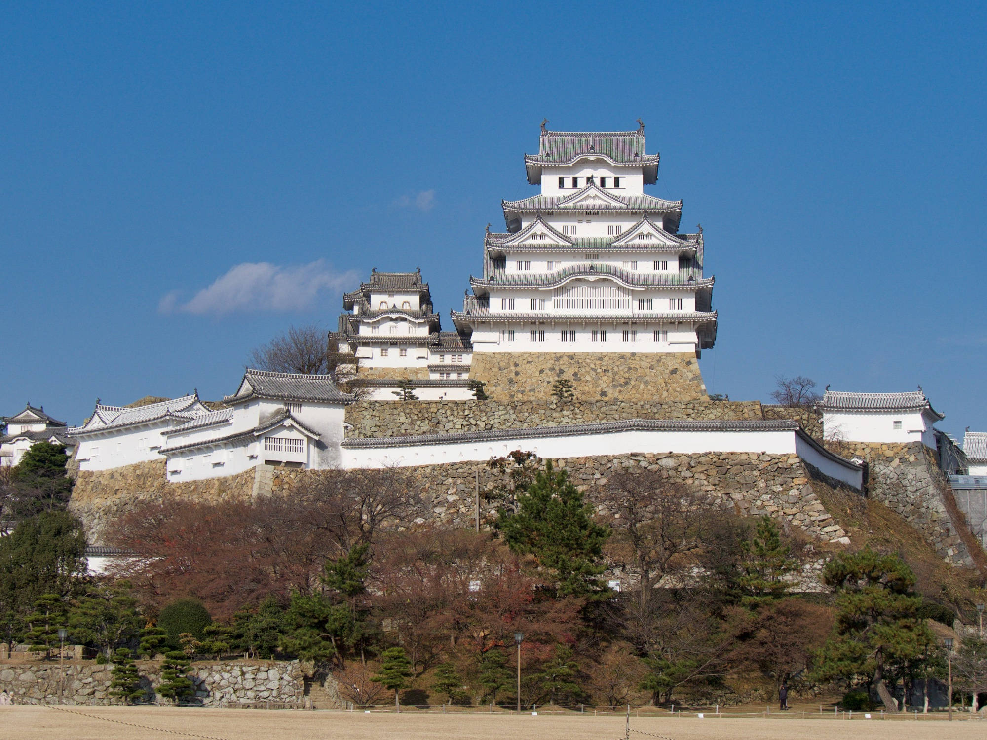 Himeji Castle 桌布 壁紙 — 一座雄偉的白色日本城堡，擁有分層屋頂，矗立在石山上，天空清澈湛藍，雲朵稀疏。