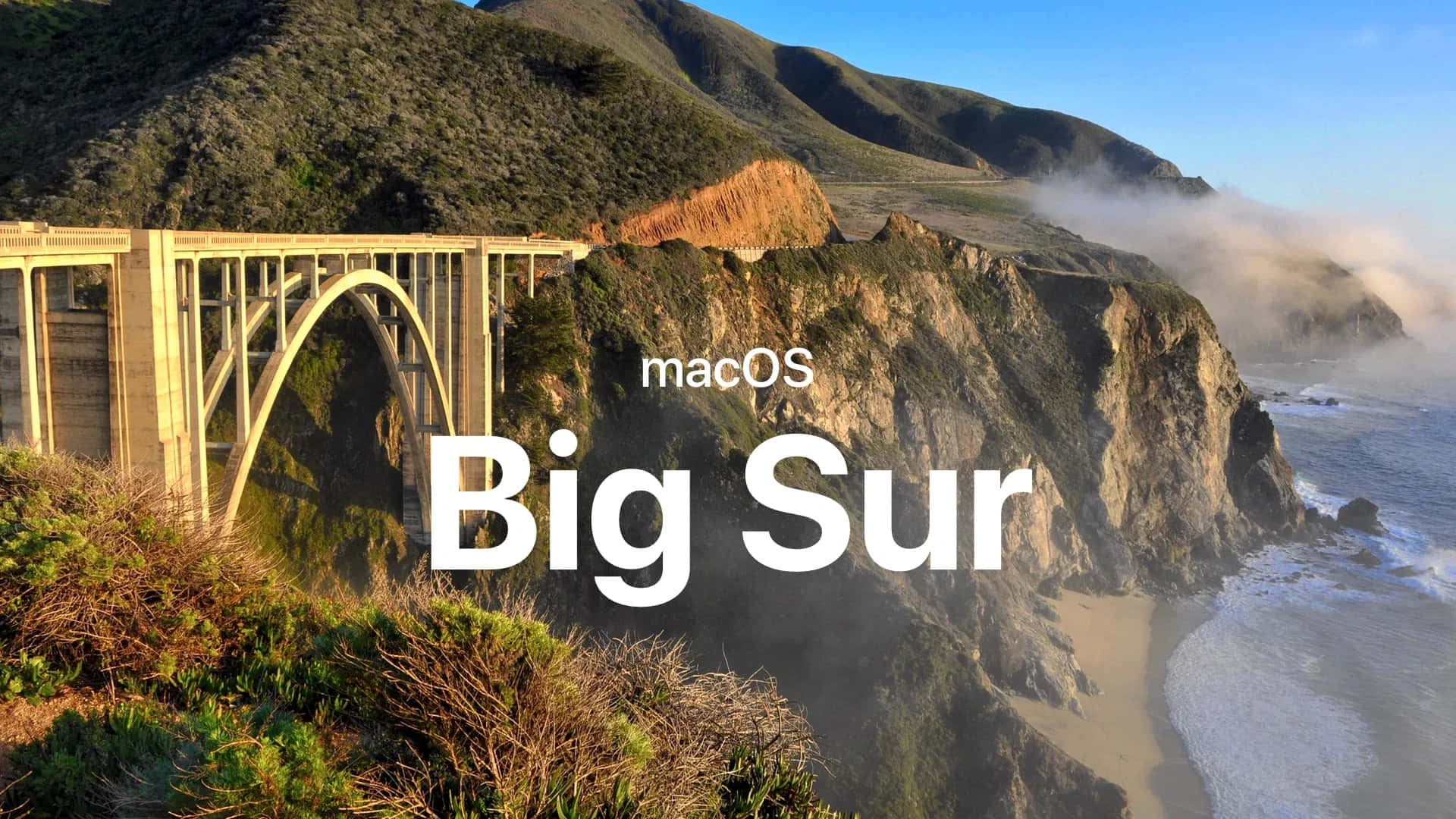 macOS Big Sur 動態桌布 桌布 壁紙 — 一座雄偉的石拱橋橫跨崎嶇的海岸懸崖，下方波濤洶湧，薄霧在晴朗的藍天下翻滾。