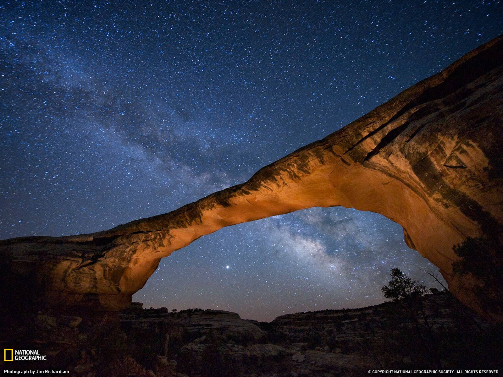 一座發光的石拱門框住繁星點點的夜空，銀河清晰可見。 — 國家地理 壁紙