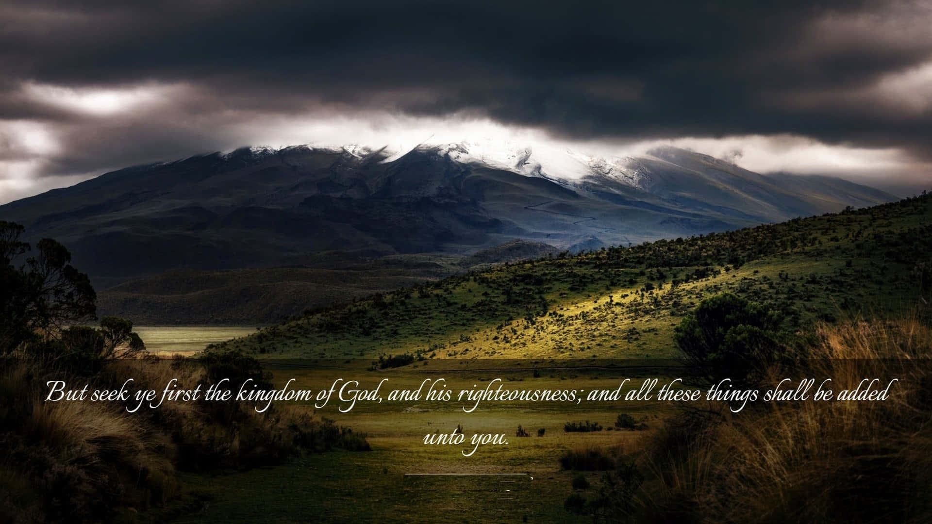 Kingdom Of God 桌布 壁紙 — 一座雄偉的雪山在戲劇性的暴風雲下聳立，金色的光芒照亮了下方長滿青草的山谷。