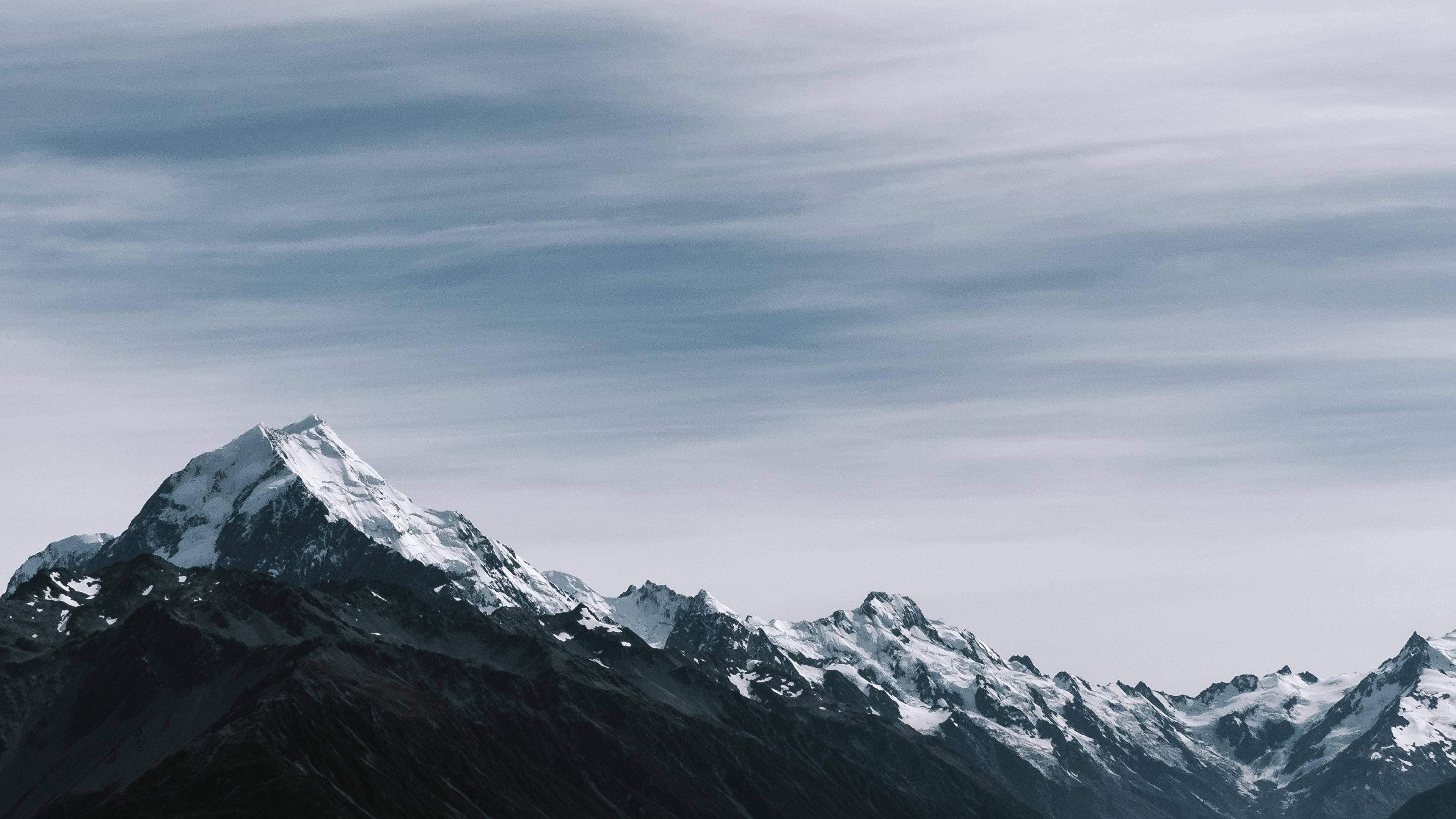 山景 桌布 壁紙 — 一座雄偉的雪山山峰在帶有條紋雲的柔和灰色天空下陡峭地聳立。