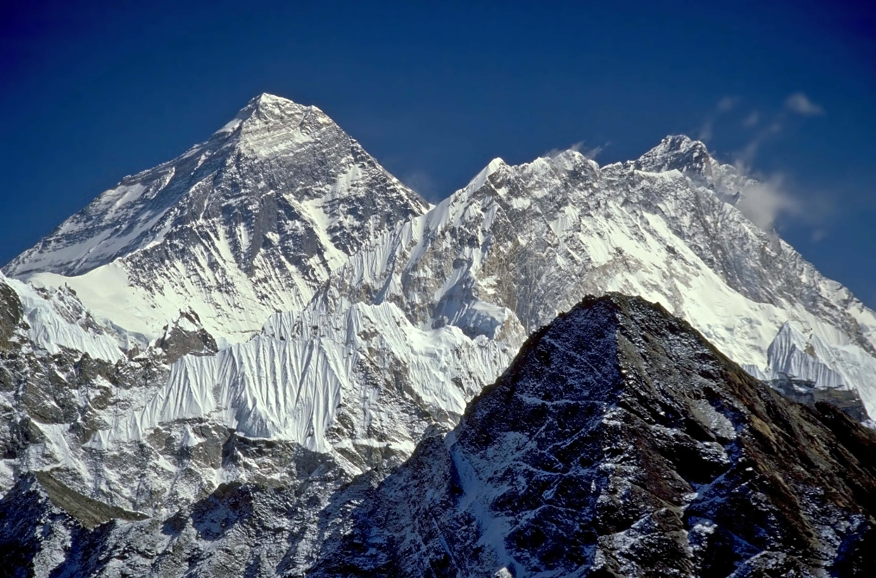 Mount Everest 桌布 壁紙 — 一座雄偉的雪山山峰在深藍色的天空和縷縷白雲中巍然聳立。