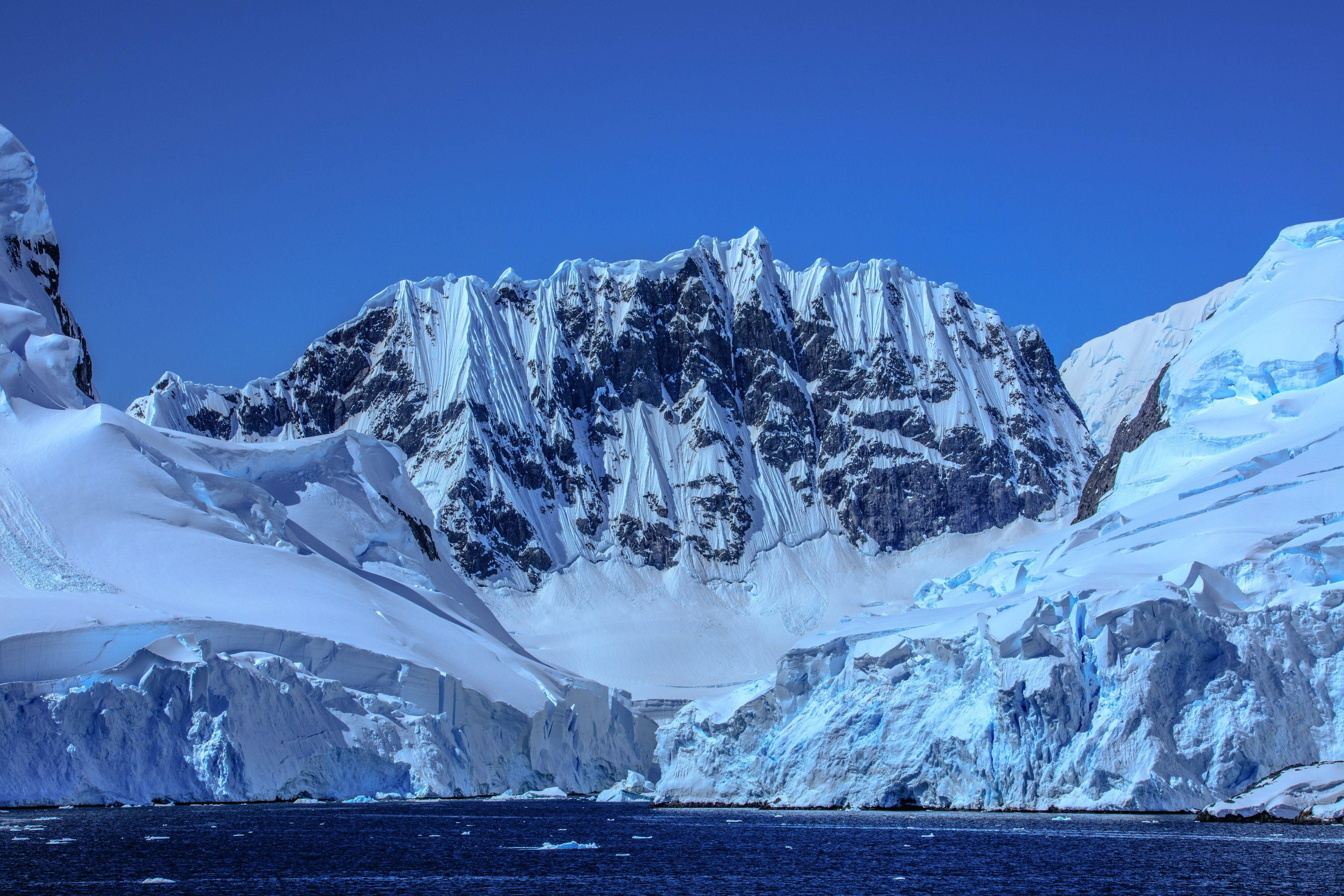 Antarctica 桌布 壁紙 — 一座雄偉的雪山山脈在清澈的藍天下從冰冷的湖水中陡峭升起。