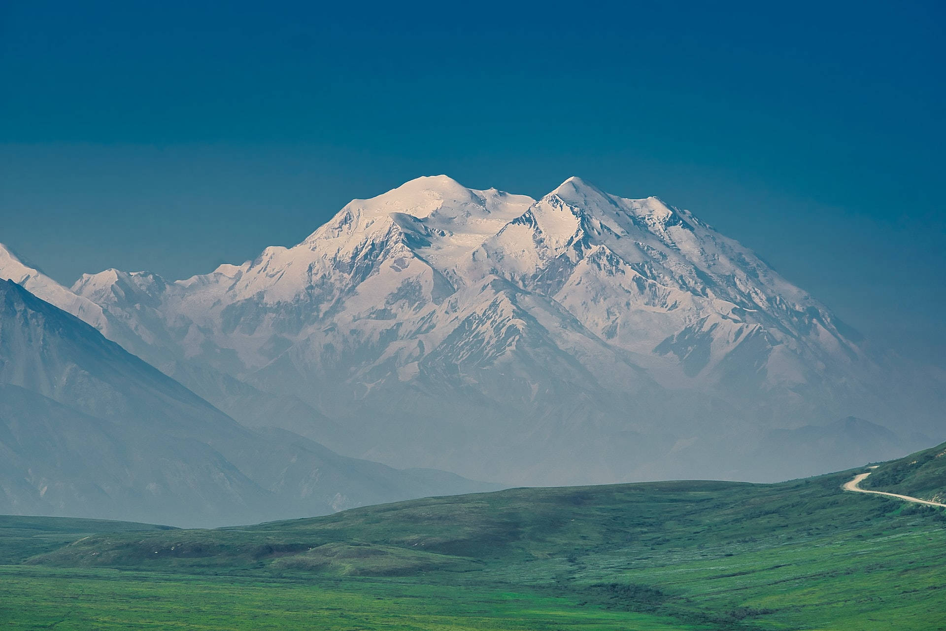 Mountain Landscape 桌布 壁紙 — 一座雄偉的雪山聳立在廣闊的綠色山谷之上，天空清澈湛藍。