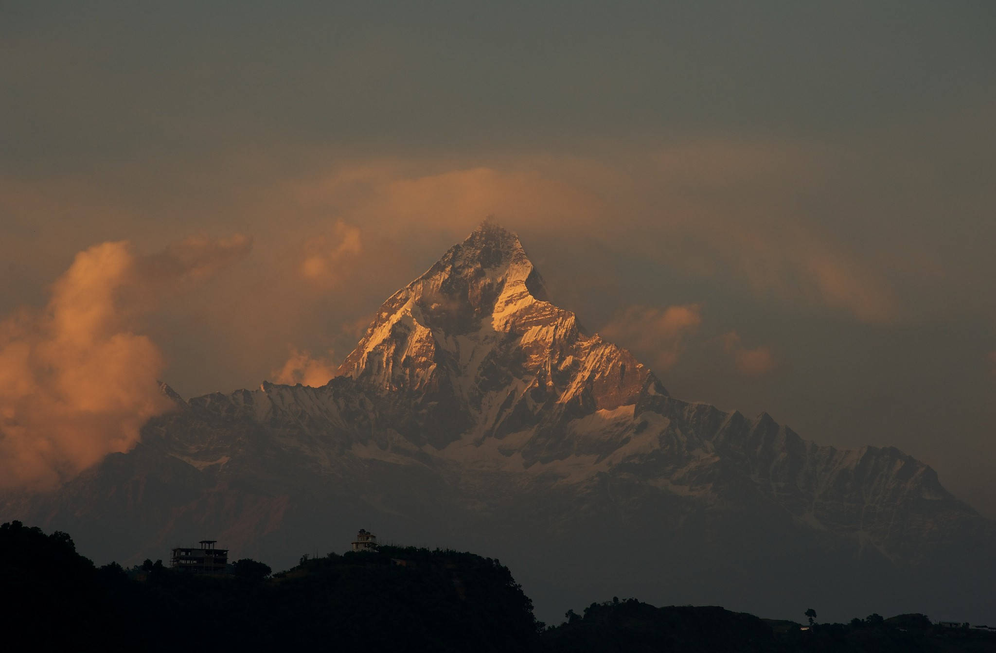 Nepal 桌布 壁紙 — 一座雄偉的雪山頂峰在日出時閃耀著金色光芒，雲霧繚繞其頂峰。