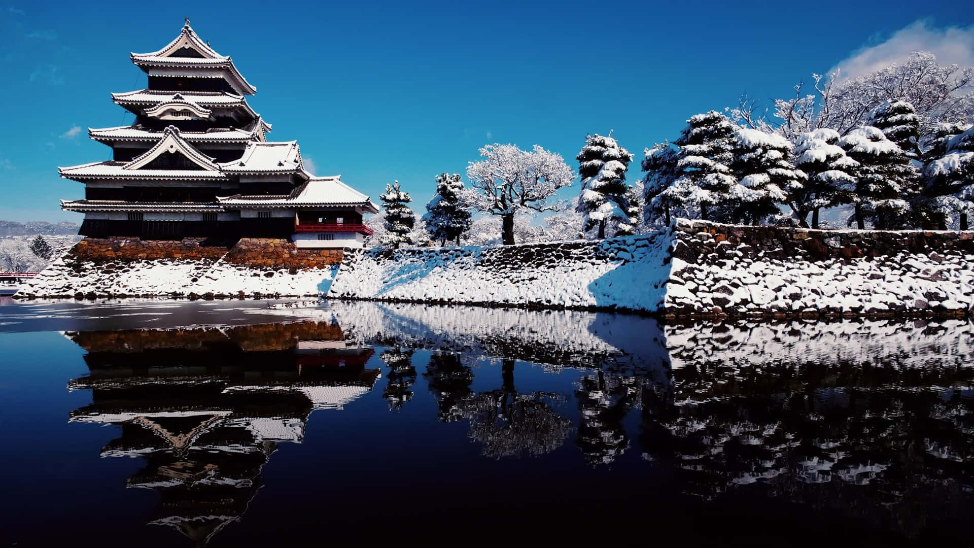 日式 桌布 壁紙 — 一座雄偉的雪覆蓋的日本城堡在平靜的水面上完美倒映，天空清澈湛藍。