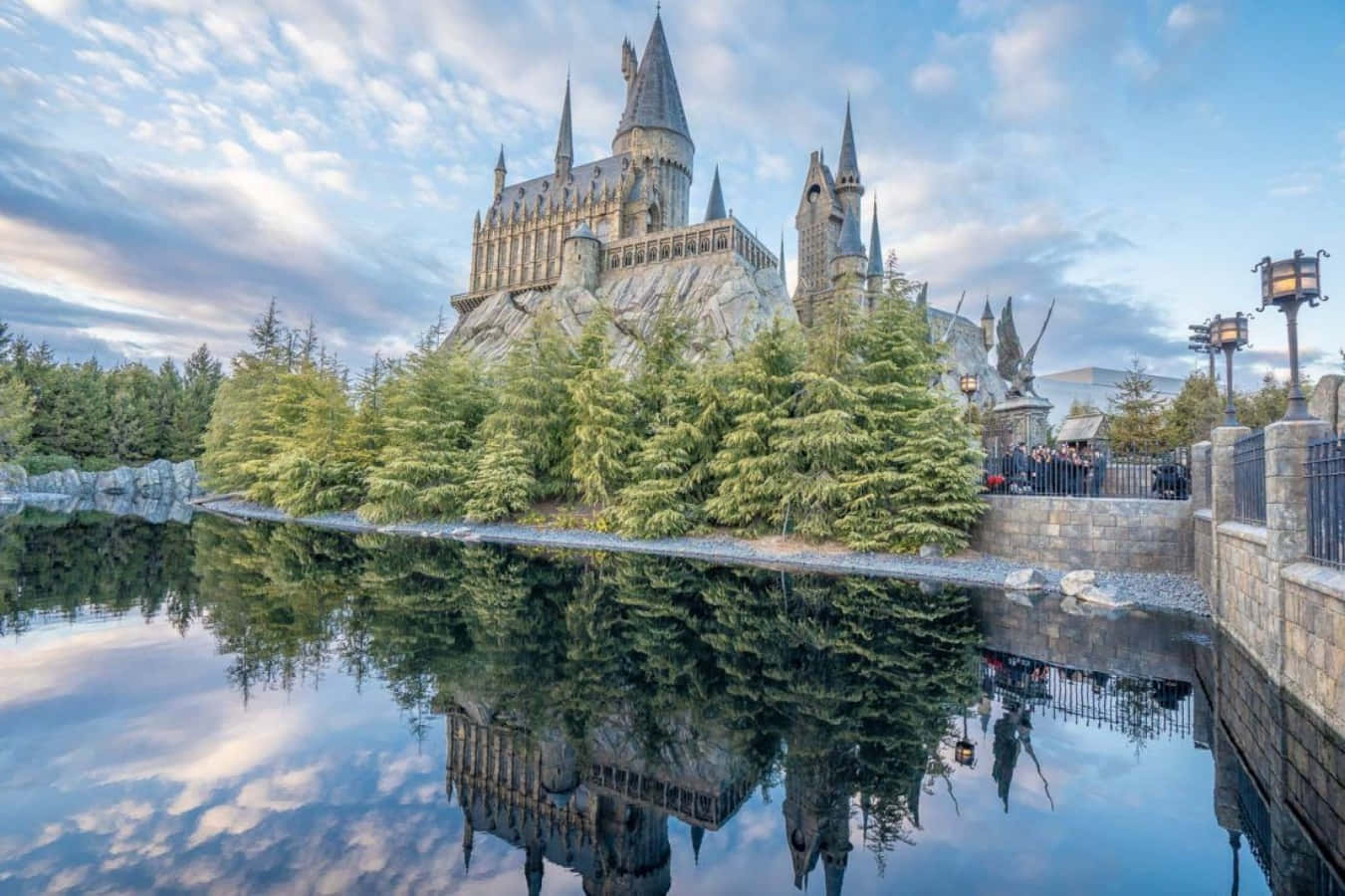 The Hogwarts Lake 桌布 壁紙 — 一座雄偉的霍格華茲城堡坐落在岩石懸崖上，其尖塔和塔樓在柔和的藍天下完美地倒映在下方平靜的水面上。