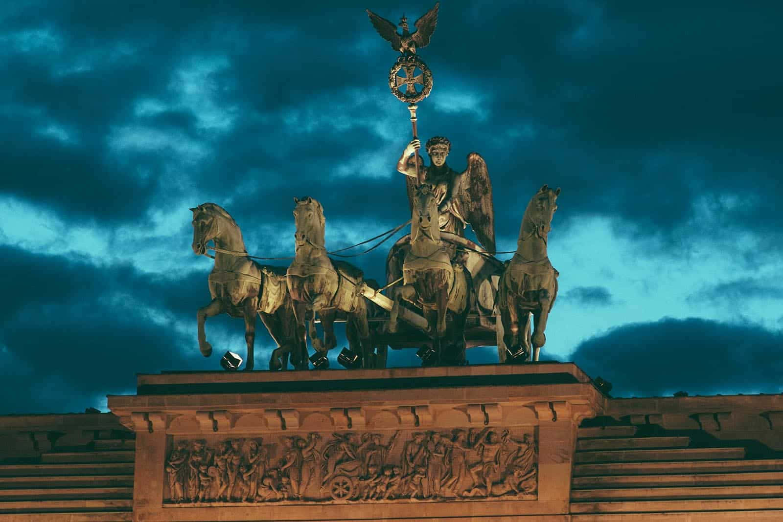 Berlin 桌布 壁紙 — 一座雄偉的青銅四馬戰車雕像，描繪一位帶翼人物手持頂端有鷹的權杖，背景是戲劇性的黃昏天空。