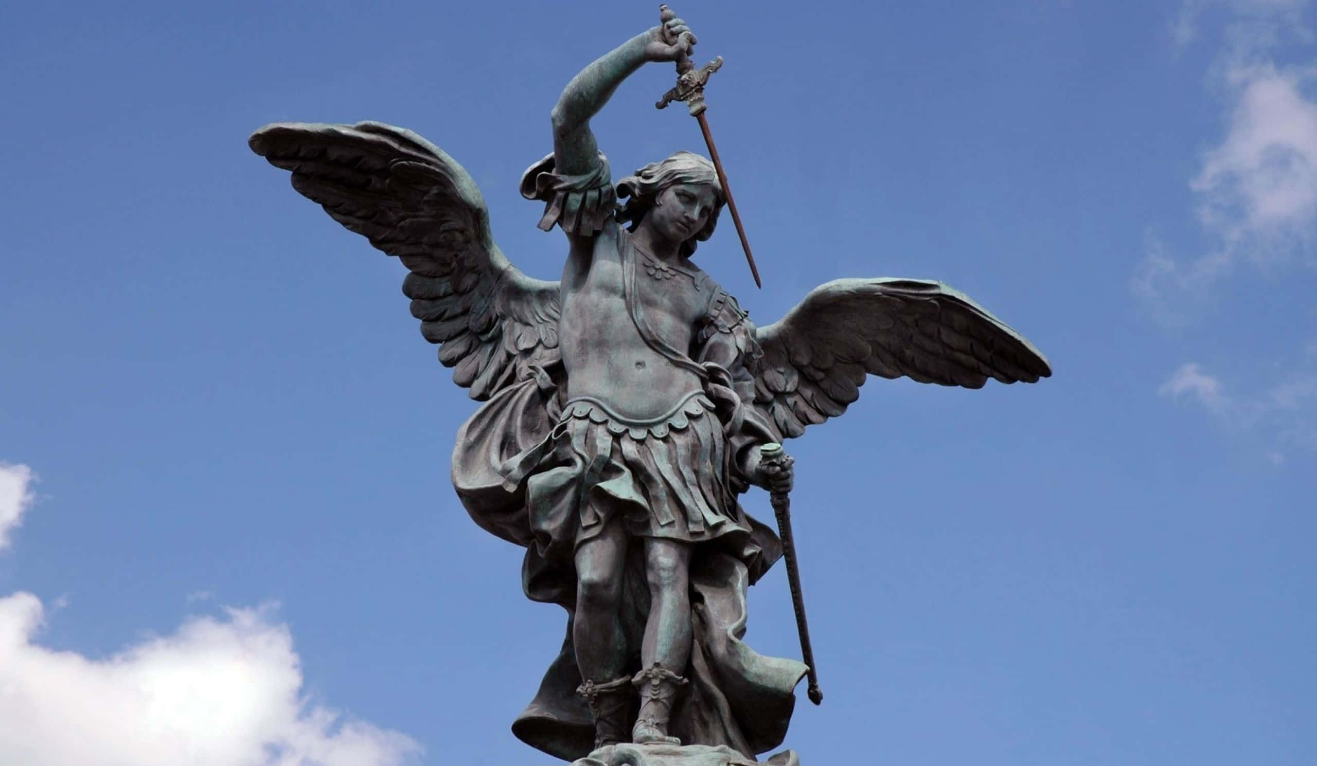Saint Michael 桌布 壁紙 — 一座雄偉的青銅天使雕像，展開翅膀，高舉寶劍，矗立在藍天白雲之下。