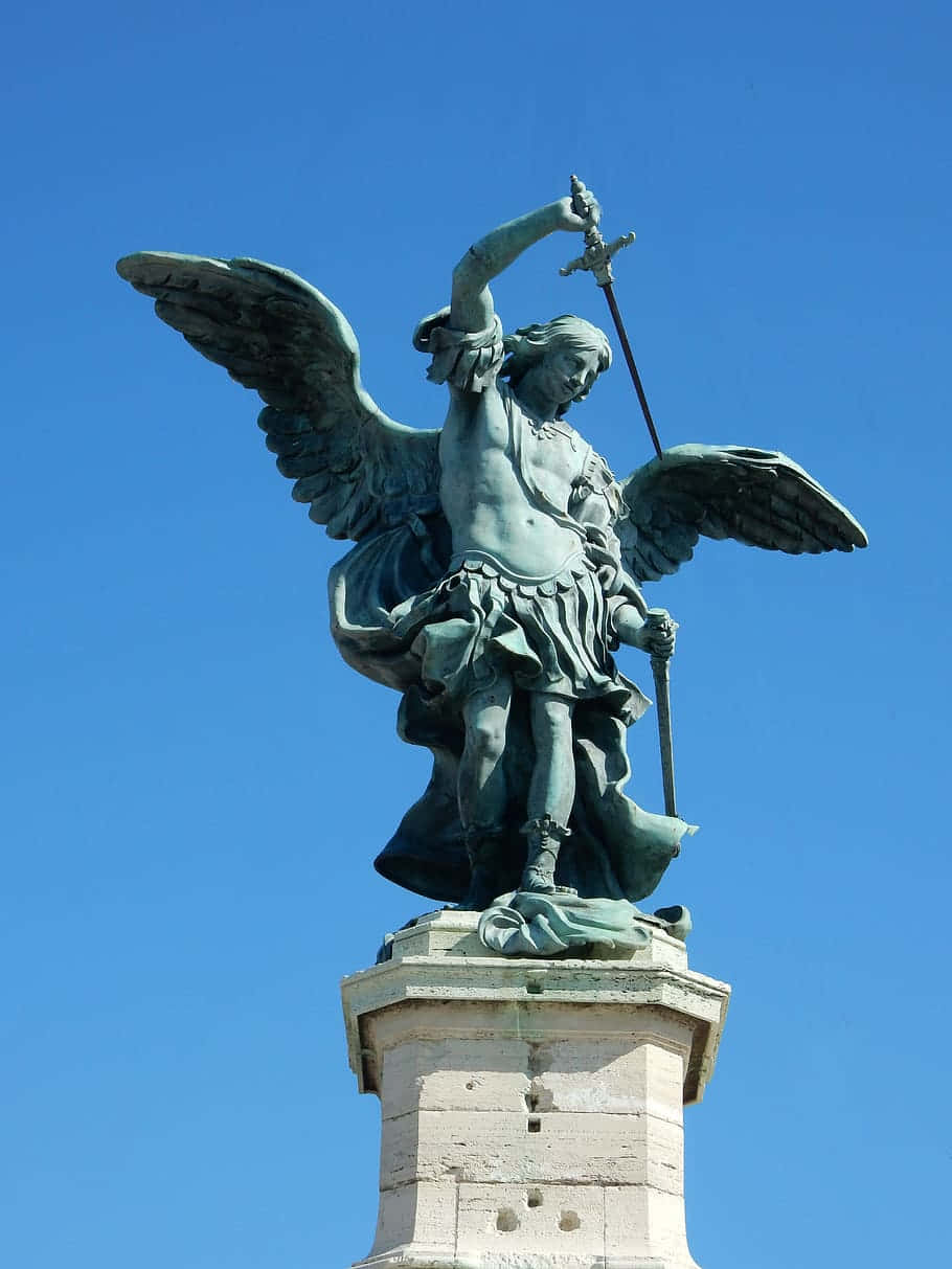 Saint Michael 桌布 壁紙 — 一座雄偉的青銅天使雕像，展開翅膀，高舉寶劍，矗立在石基座上，背景是清澈的藍天。