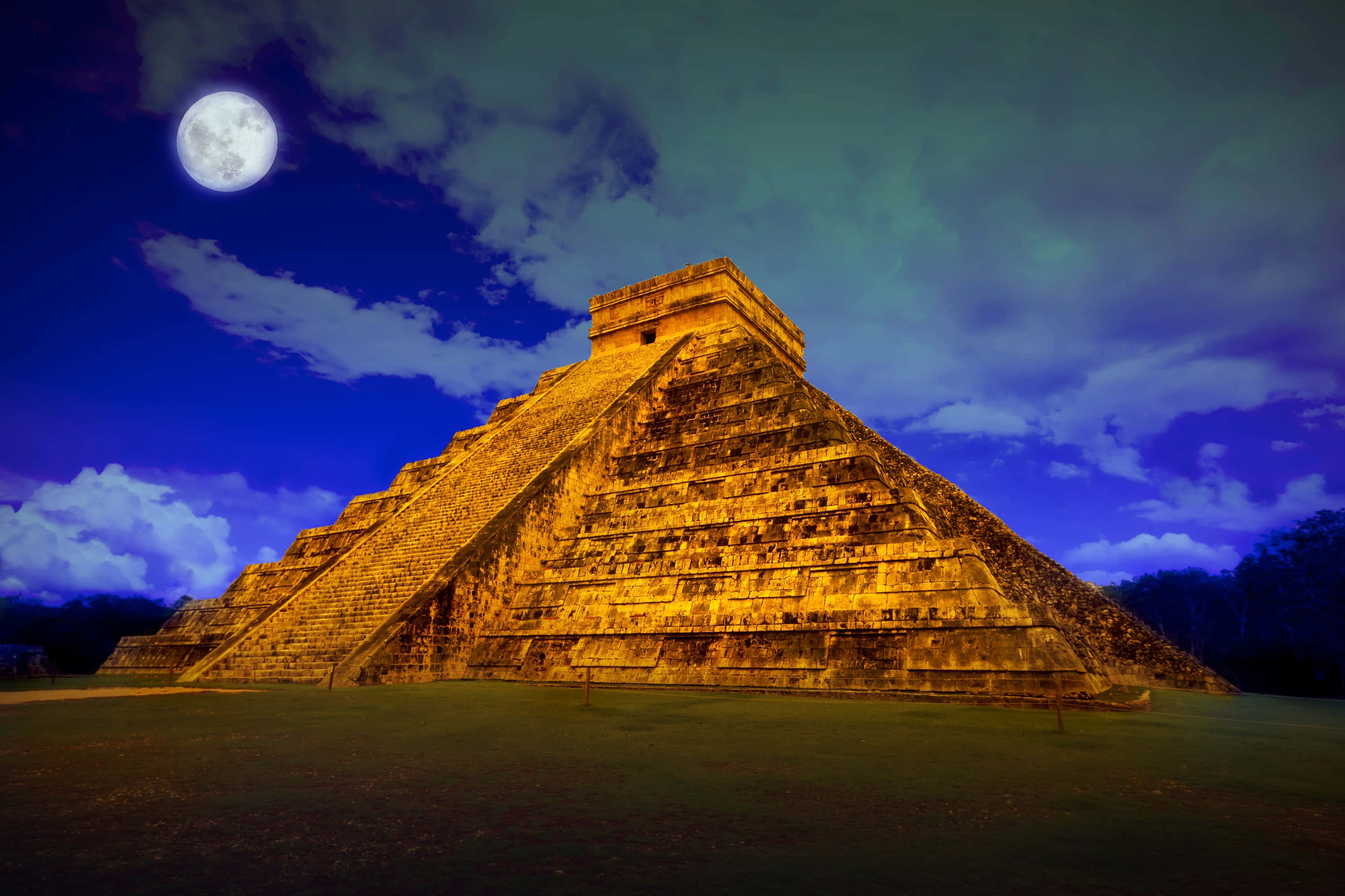 pyramid 桌布 壁紙 — 一座雄偉的馬雅金字塔沐浴在金黃色光芒中，下方是戲劇性的月光天空，雲朵翻湧。
