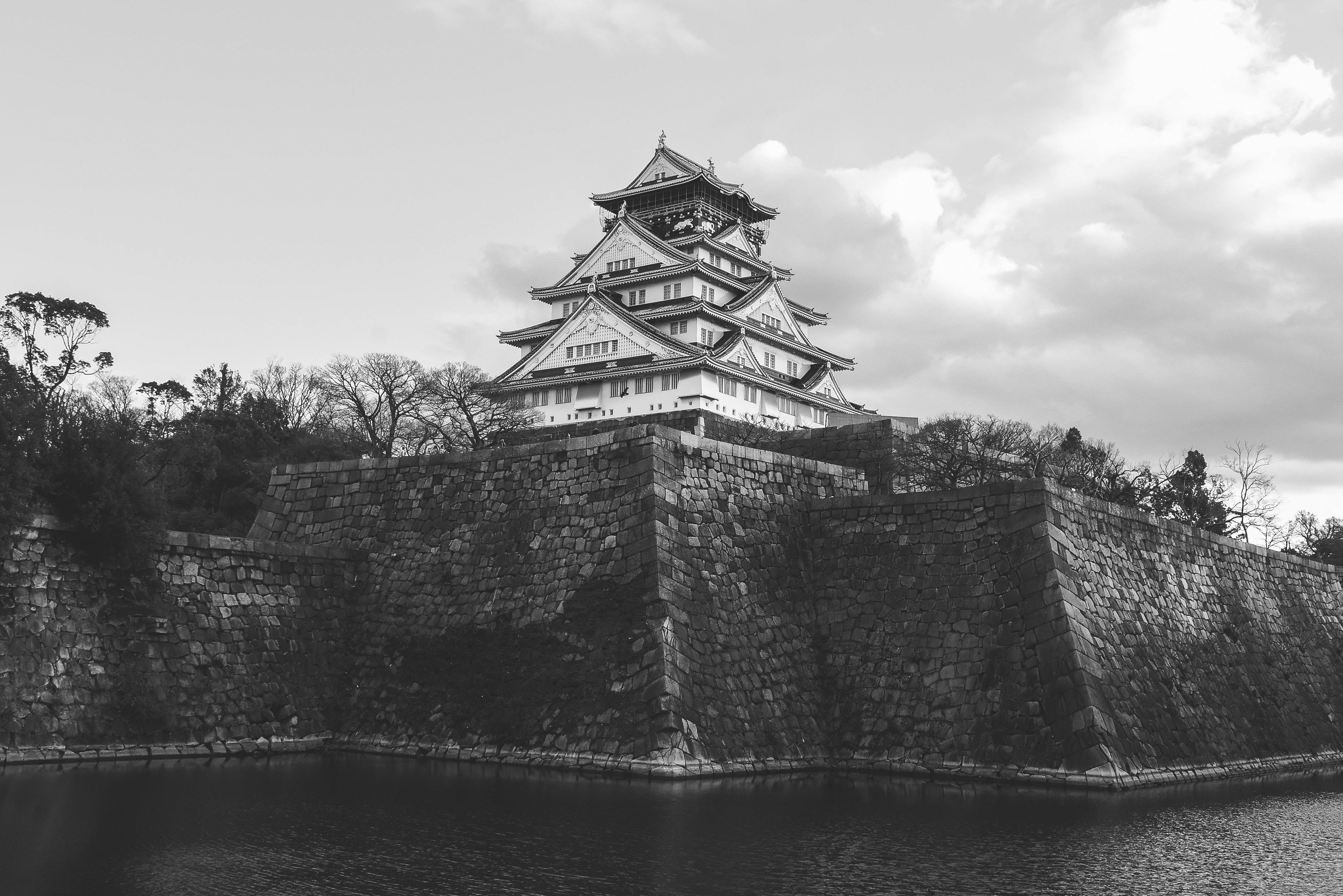 Osaka Castle 桌布 壁紙 — 一座雄偉的黑白城堡在陰天之下聳立於石牆和寧靜的護城河之上。