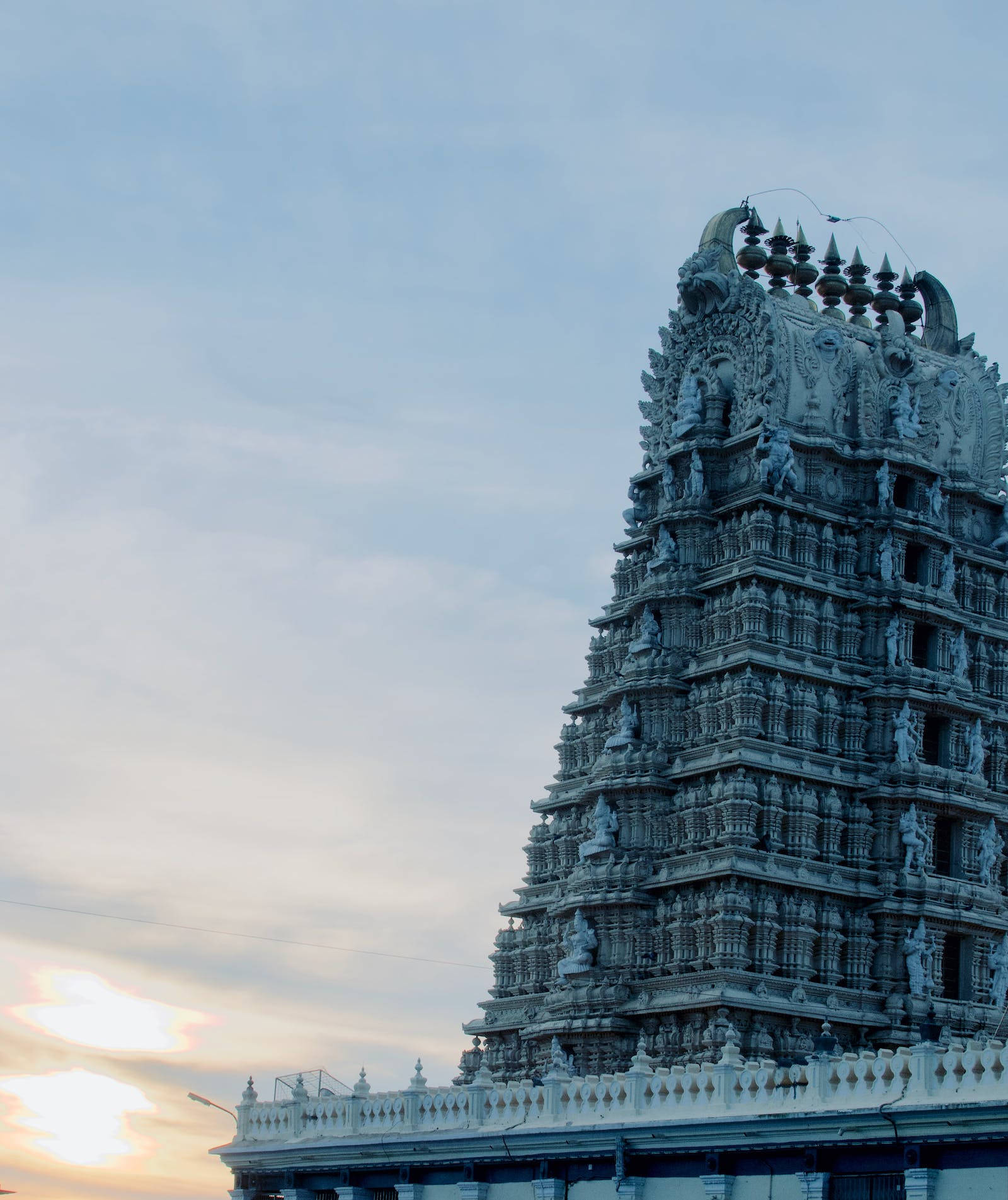 Hindu Temple 桌布 壁紙 — 一座雕刻精細的高聳寺廟塔門（gopuram）在柔和的暮色天空中升起，溫暖的陽光穿過雲層。