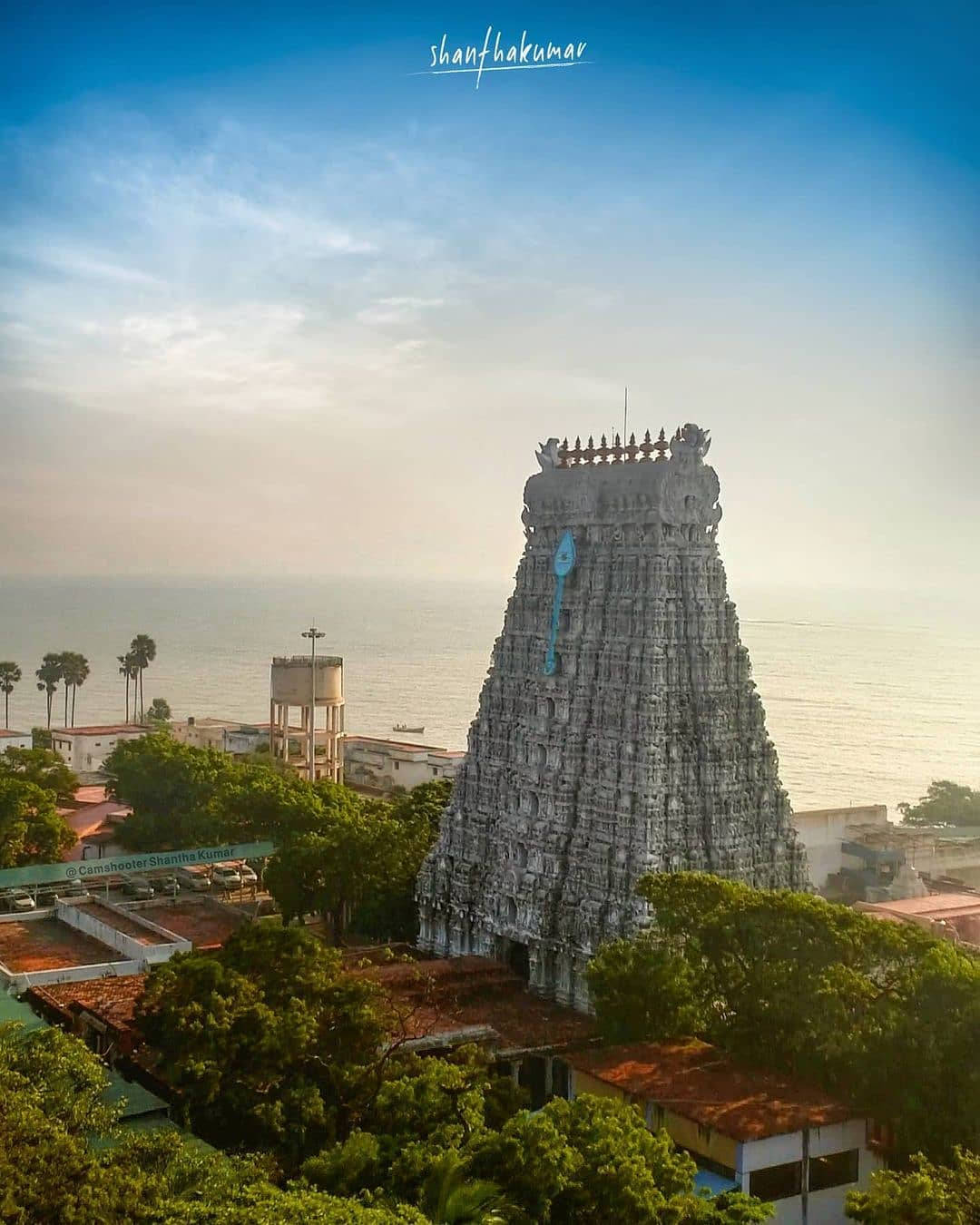 Hindu Temple 桌布 壁紙 — 一座雕刻精美的高聳印度教寺廟，在柔和的金色日落天空下，聳立於海邊茂密的綠樹之上。