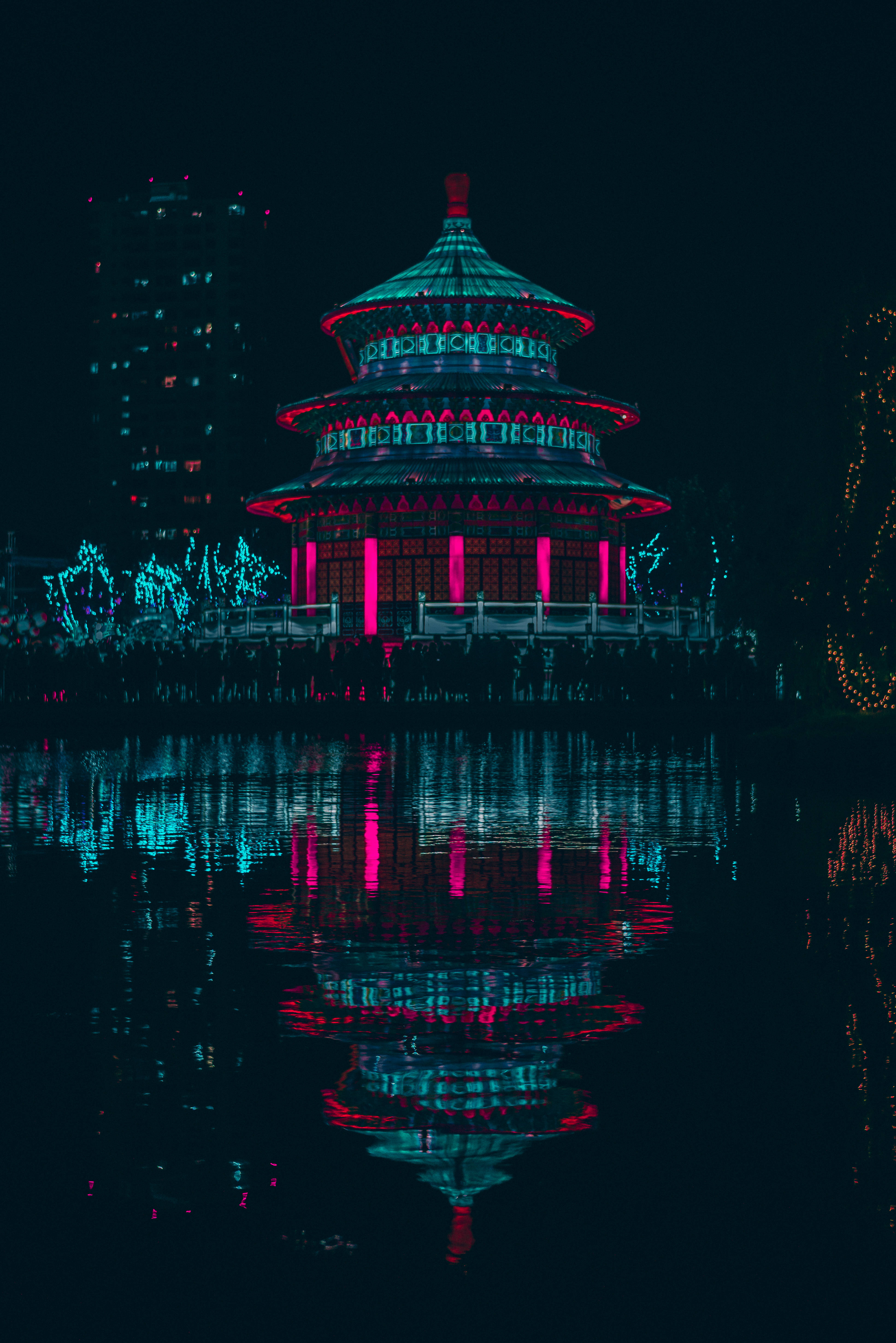 賽博龐克超寬 桌布 壁紙 — 一座霓虹燈照亮的傳統寶塔在夜空下倒映在暗水中，背景是閃爍的城市燈光。