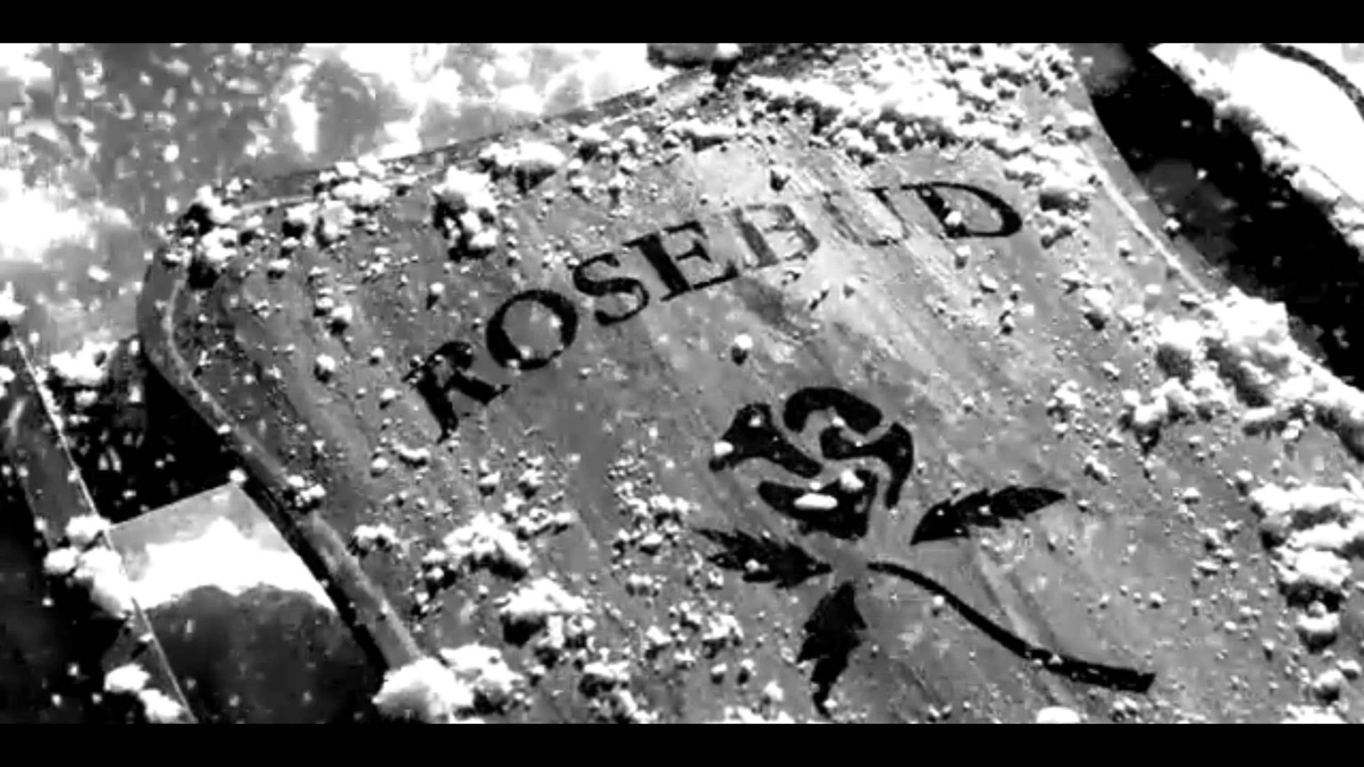Citizen Kane 桌布 壁紙 — 一座風化的墓碑，刻有「ROSEBUD」和玫瑰徽章，在陰天覆蓋著白雪。