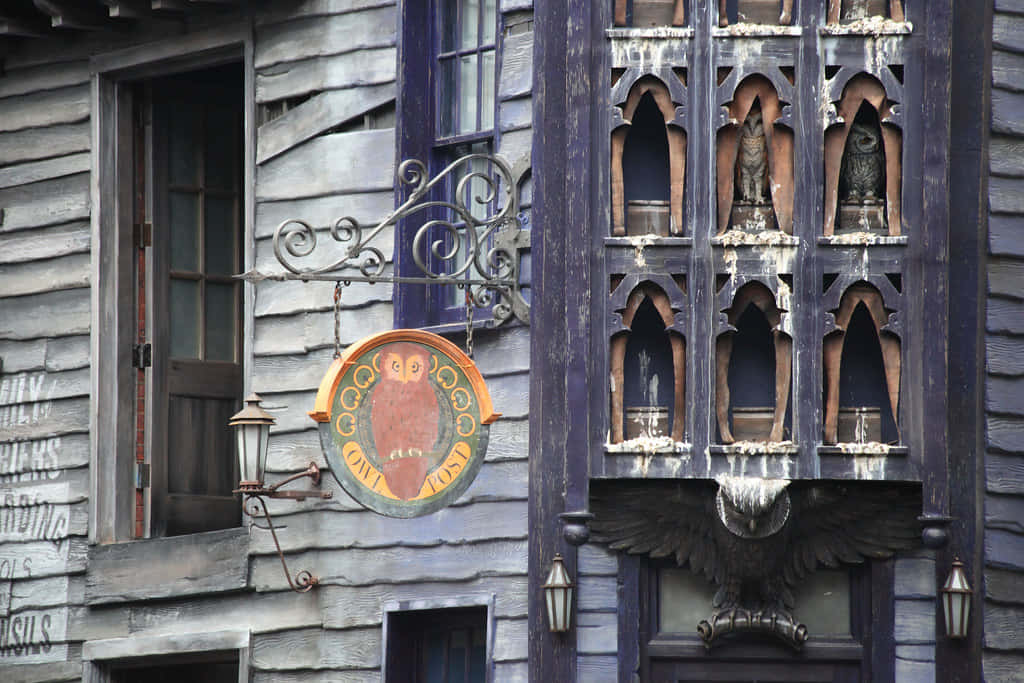 The Hogwarts Owlery 桌布 壁紙 — 一座風化的木建築有一個圓形貓頭鷹標誌和哥德式壁龕，內有貓頭鷹雕像，下方有一個大型鷹雕塑。