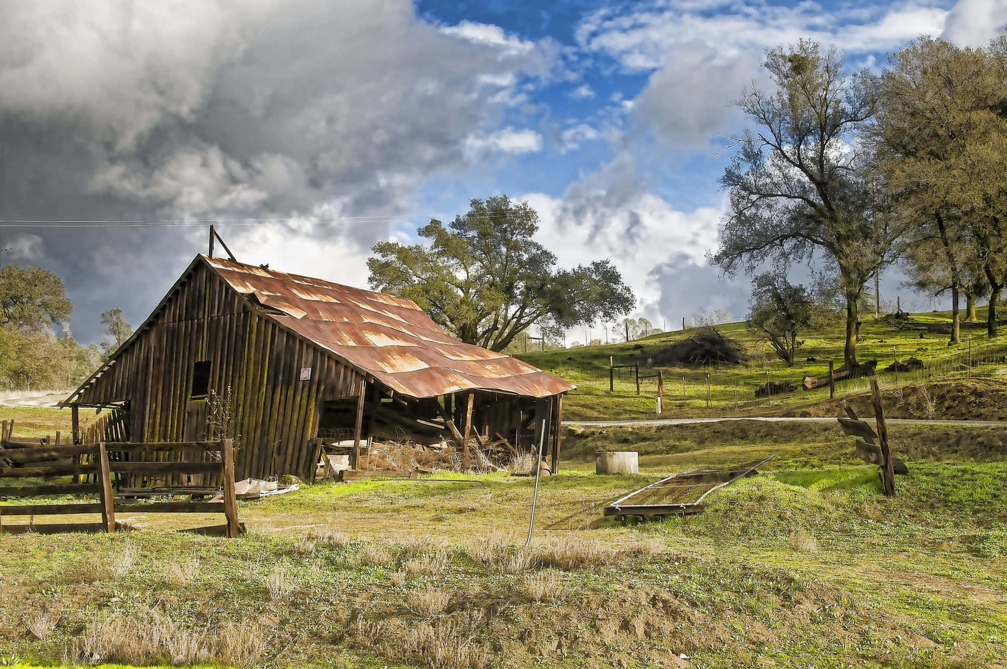 Old Farm 桌布 壁紙 — 一座風化的木製穀倉，帶有生鏽的屋頂，獨自矗立在草地田野中，天空烏雲密布，氣氛戲劇化。