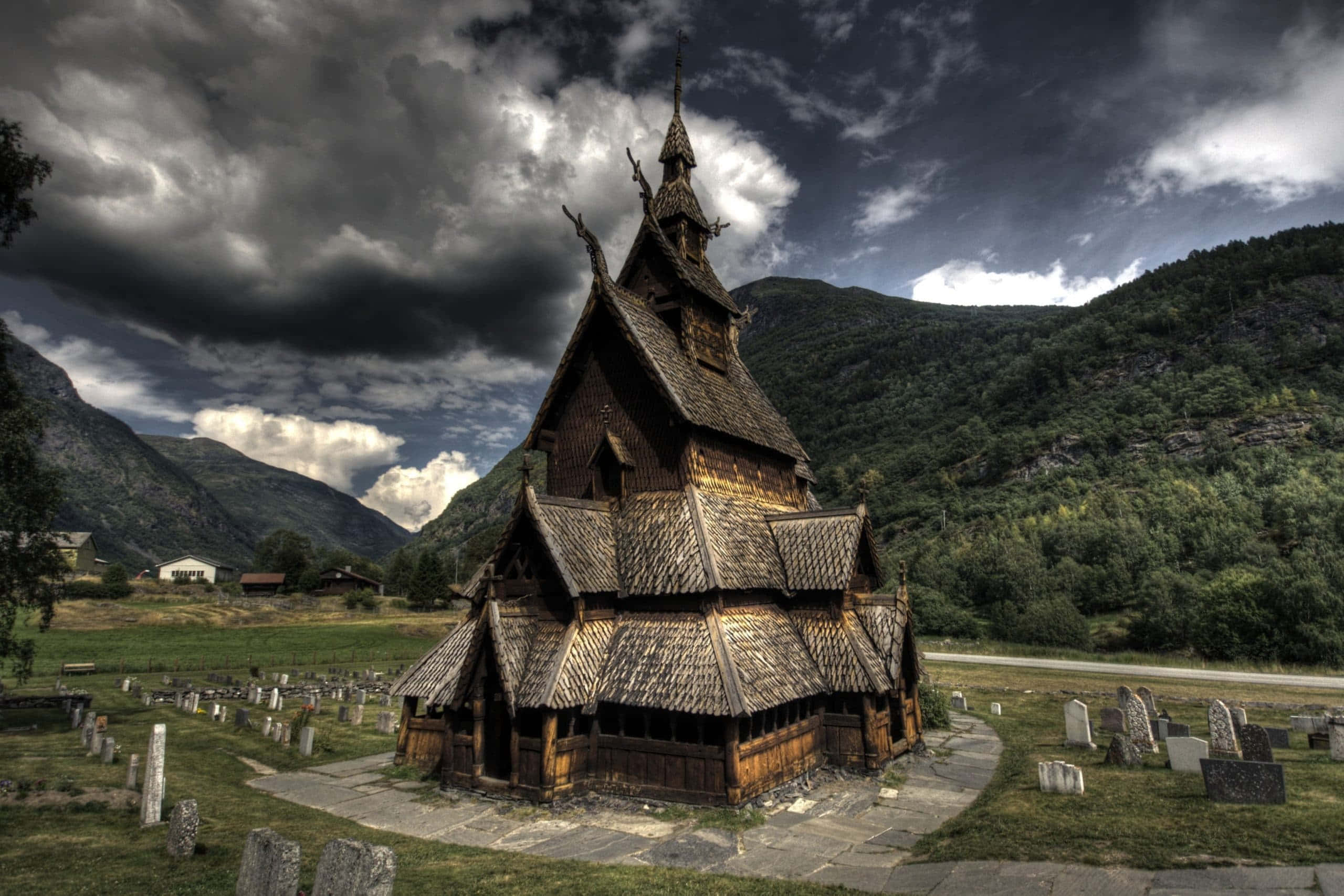Norway 桌布 壁紙 — 一座風化的木造木板教堂在戲劇性的暴風雨天空下莊嚴地矗立，背景有山脈。