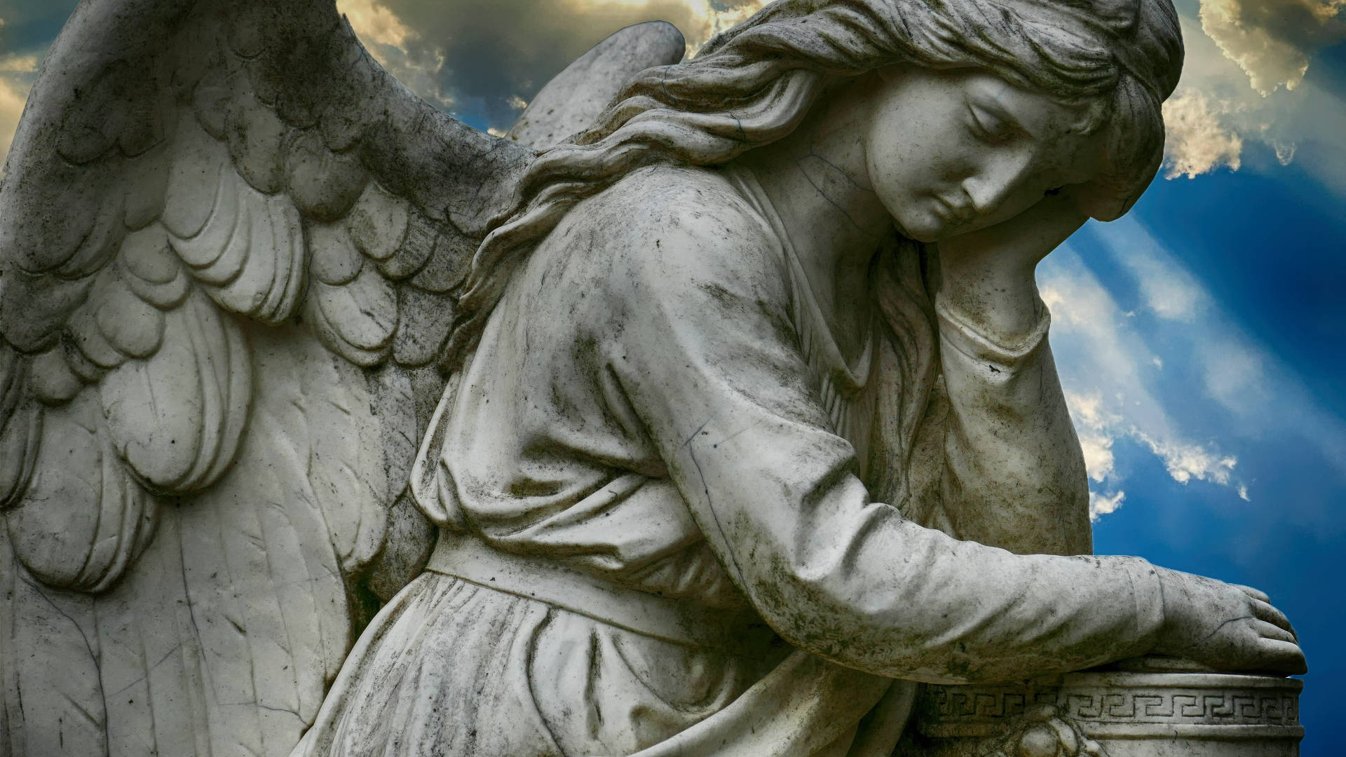 angels 桌布 壁紙 — 一座風化的石天使雕像，帶有精細的翅膀，悲傷地將頭靠在戲劇性的藍天和陽光下。