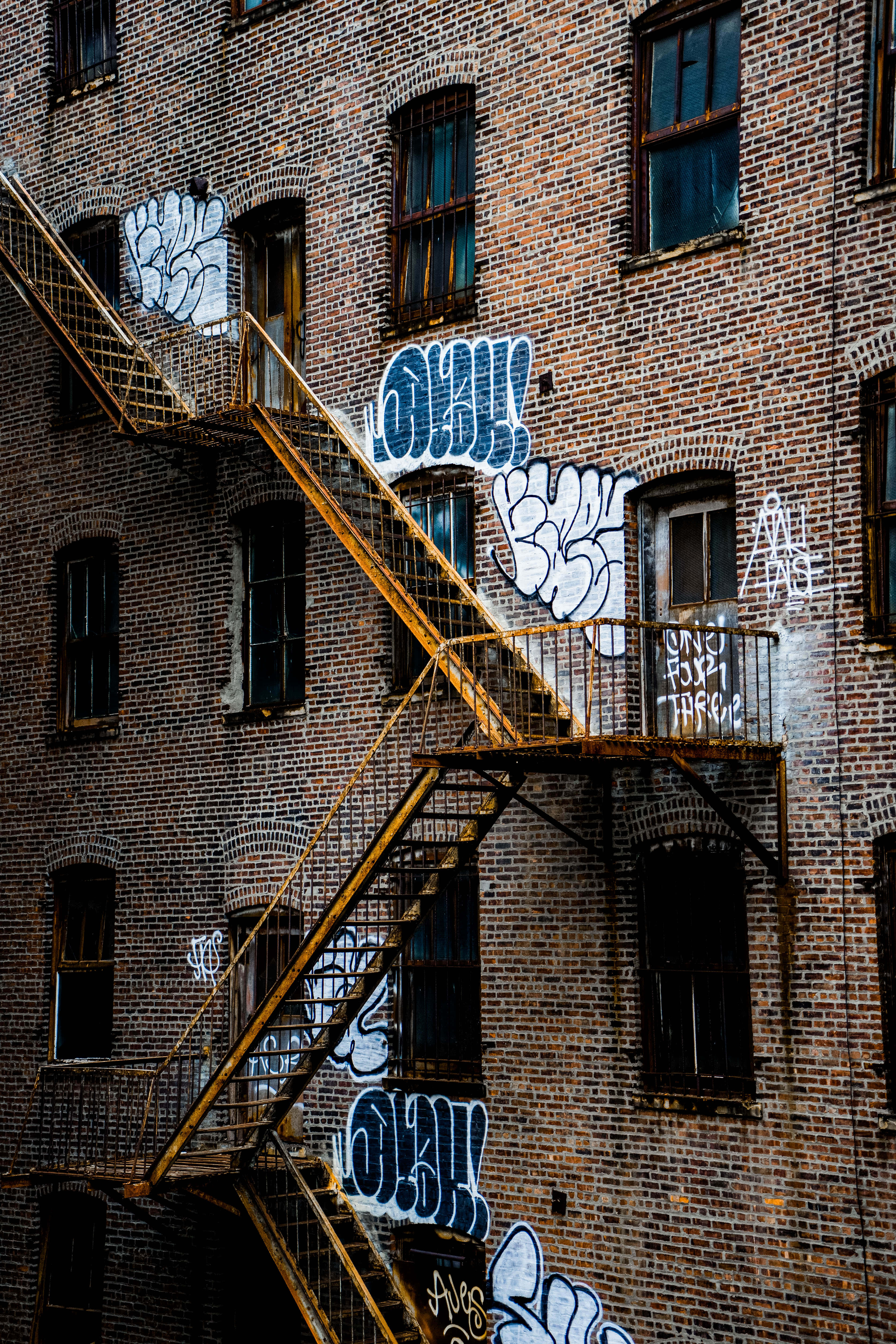 Brick Wall 桌布 壁紙 — 一座風化的磚砌建築，覆蓋著鮮豔的塗鴉，生鏽的防火梯蜿蜒而上。