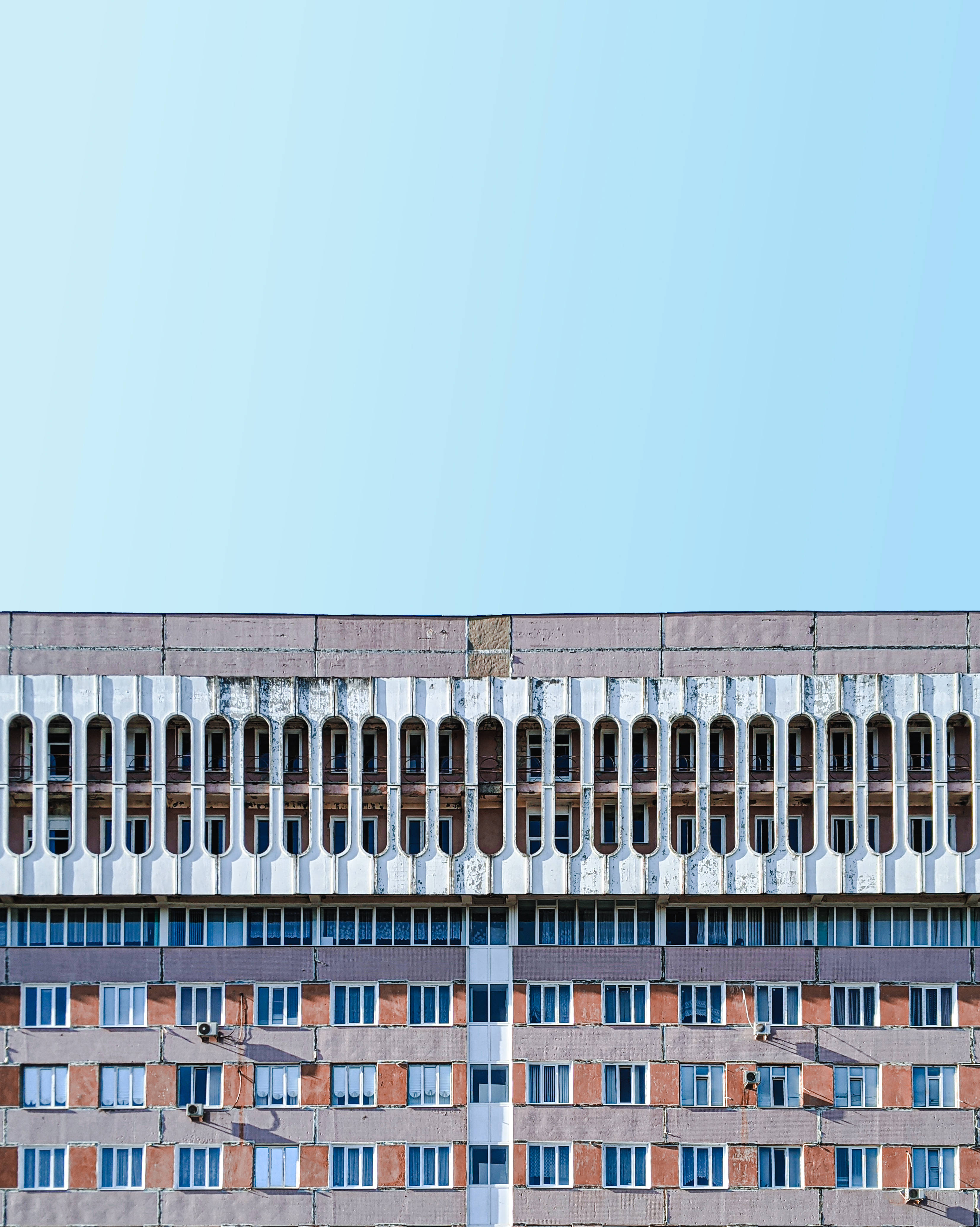 Moldova 桌布 壁紙 — 一座風化的粗獷主義公寓大樓，帶有重複的拱形窗戶，矗立在清澈的淡藍色天空下。