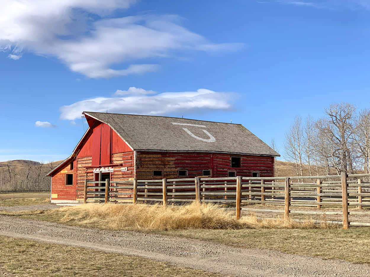 Farmhouse 桌布 壁紙 — 一座風化的紅色木製穀倉，屋頂上繪有一個大型白色「U」，矗立在晴朗藍天和零星白雲之下。