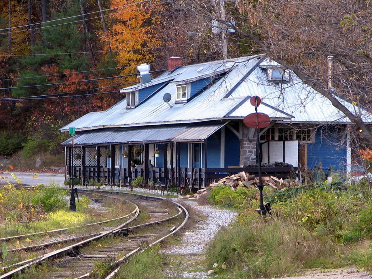 Train Station 桌布 壁紙 — 一座風化的藍色火車站，帶有波紋金屬屋頂，坐落在被秋葉環繞的彎曲鐵軌旁。