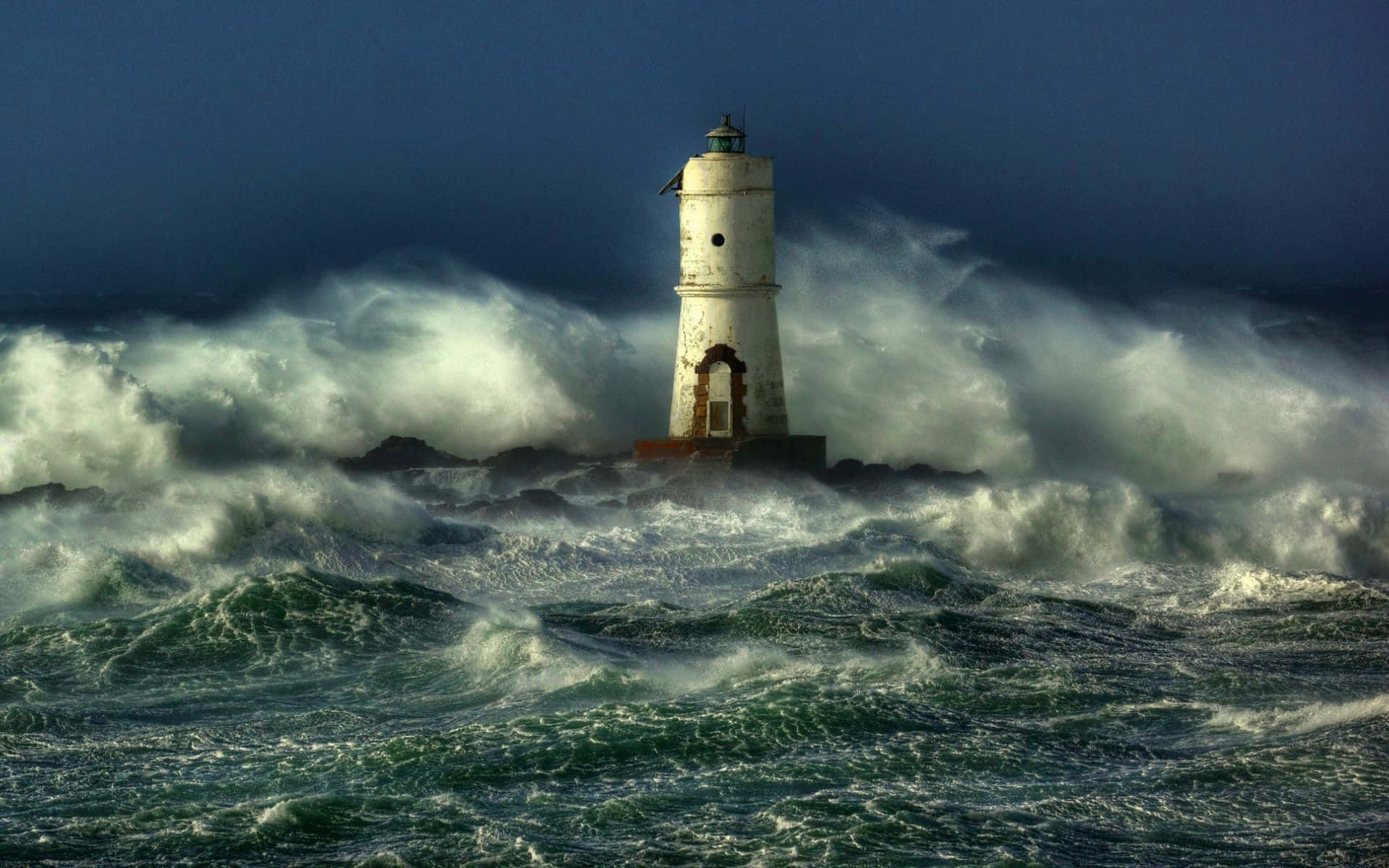 Ocean Storm 桌布 壁紙 — 一座飽經風霜的燈塔在陰暗的天空下，頑強地抵禦著洶湧的暴風海浪。