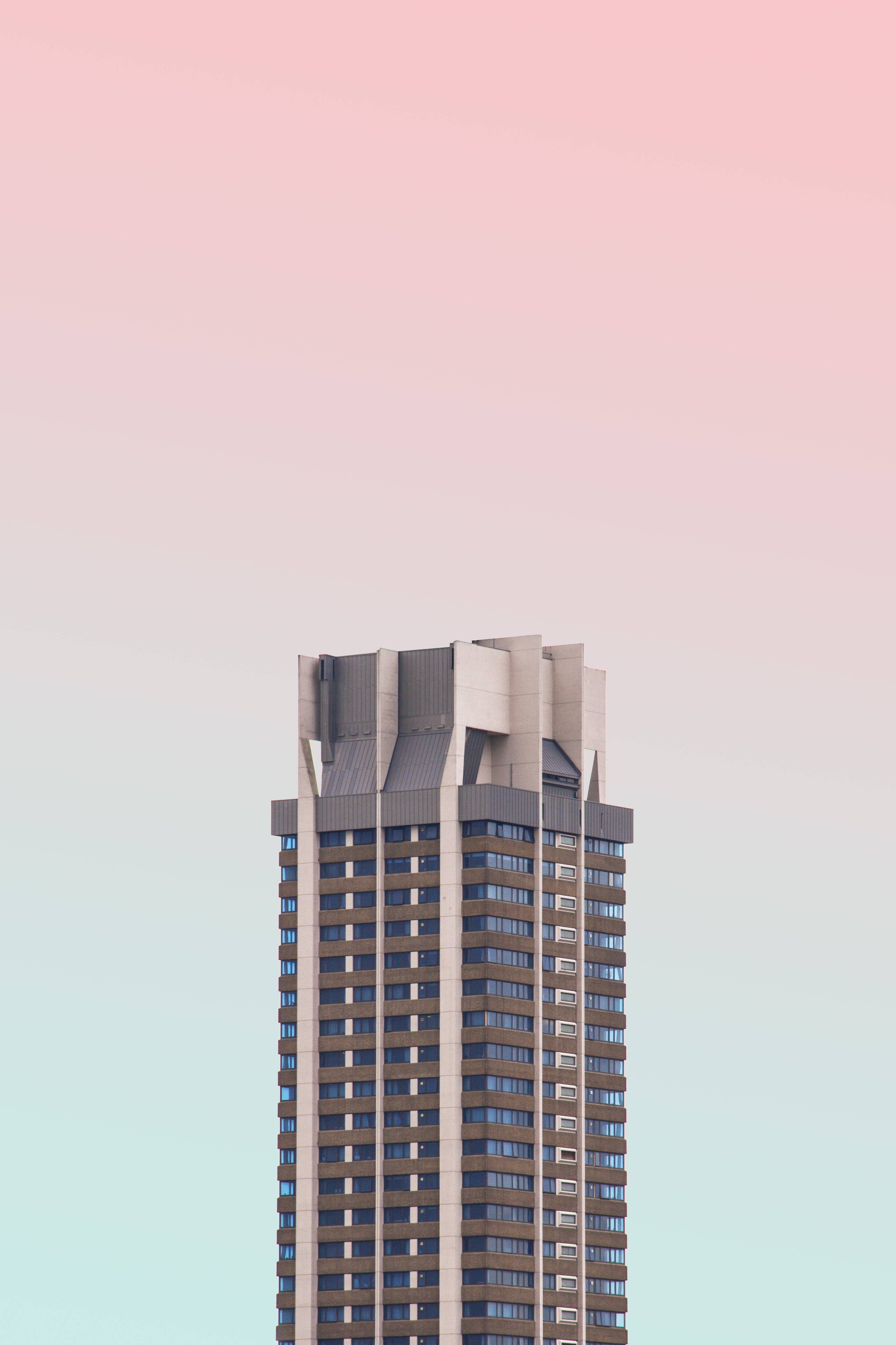 Skyscraper 桌布 壁紙 — 一座高大的現代主義摩天大樓在柔和的粉紅色和薄荷綠色漸變天空中升起。