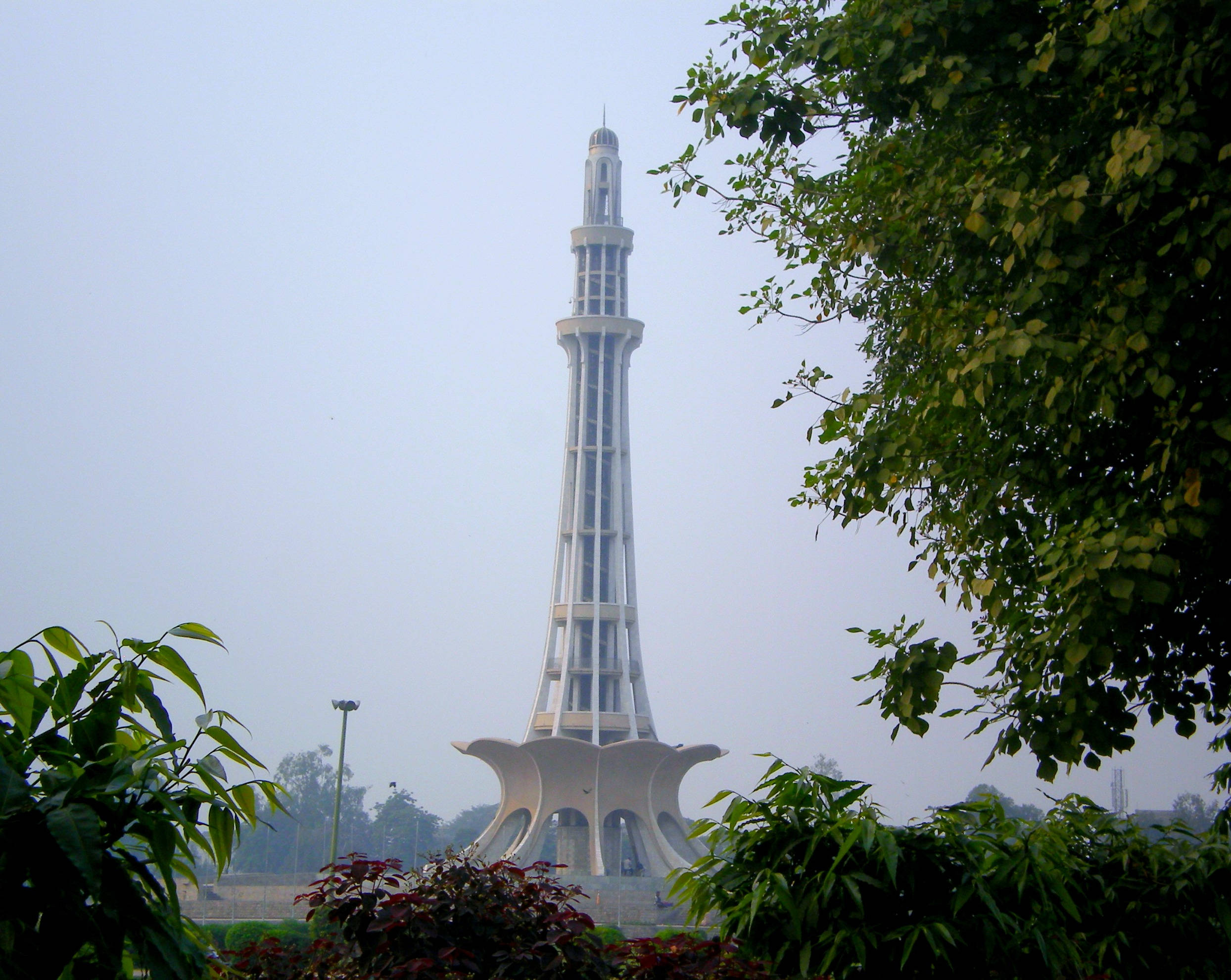 Pakistan 桌布 壁紙 — 一座高大的白色宣禮塔穿過朦朧的天空，前景是茂密的綠色樹葉。