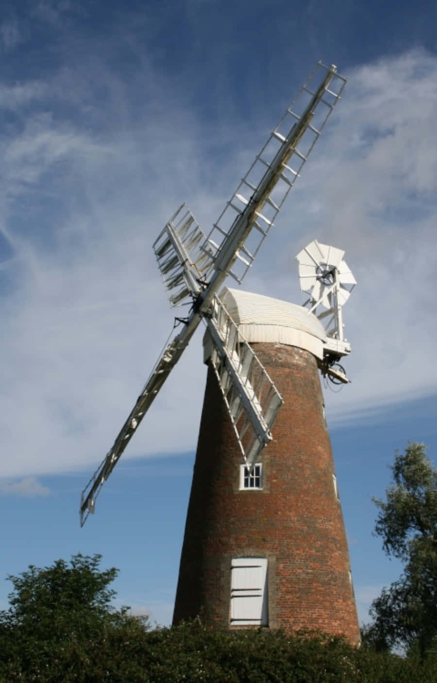 windmill 桌布 壁紙 — 一座高大的磚造風車，白色風帆，矗立在晴朗藍天和縷縷白雲下。
