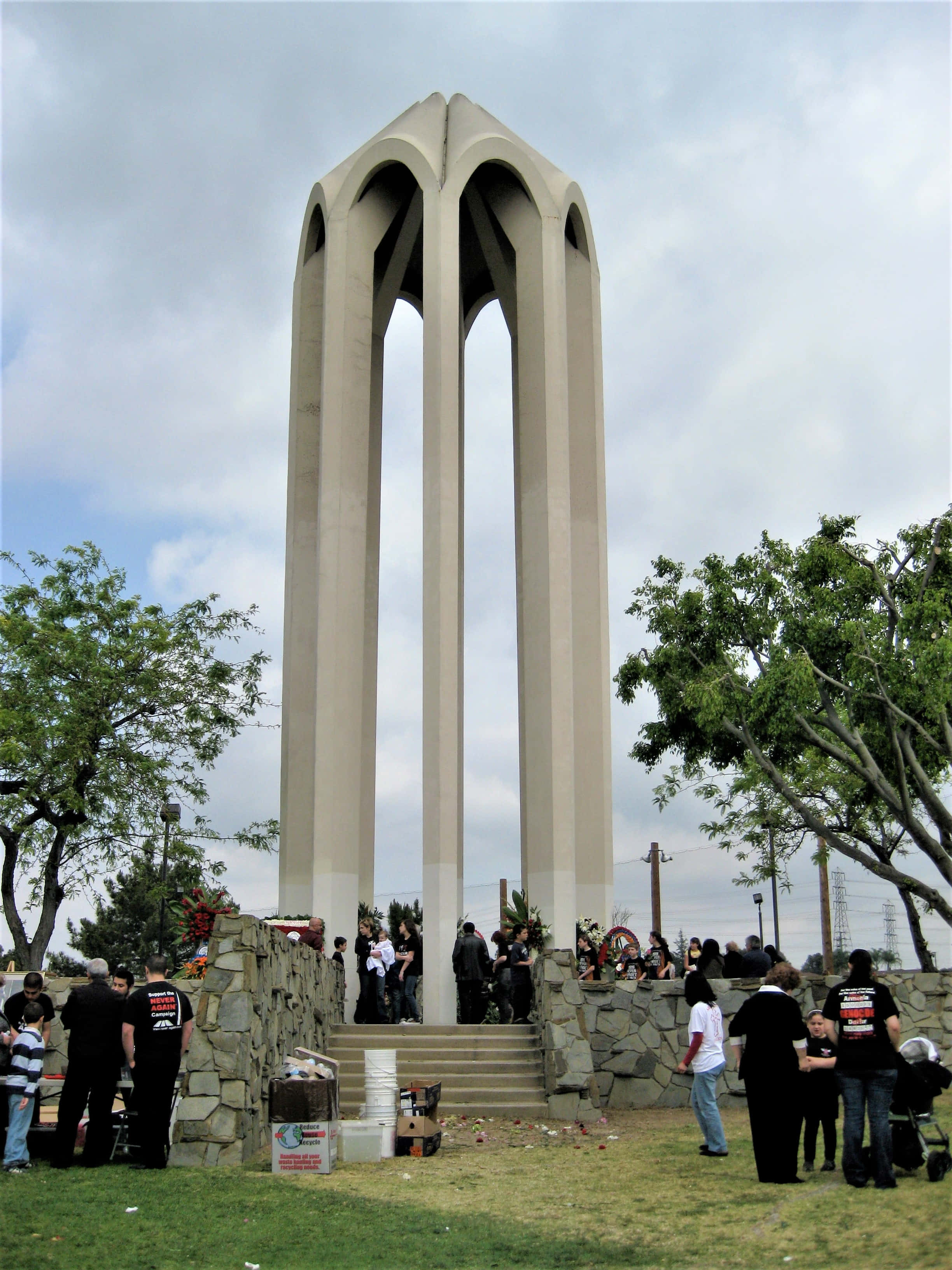 Memorial 桌布 壁紙 — 一座高大的米色紀念碑，帶有拱形開口，矗立在公園中，人們在陰天聚集在其石質底座周圍。