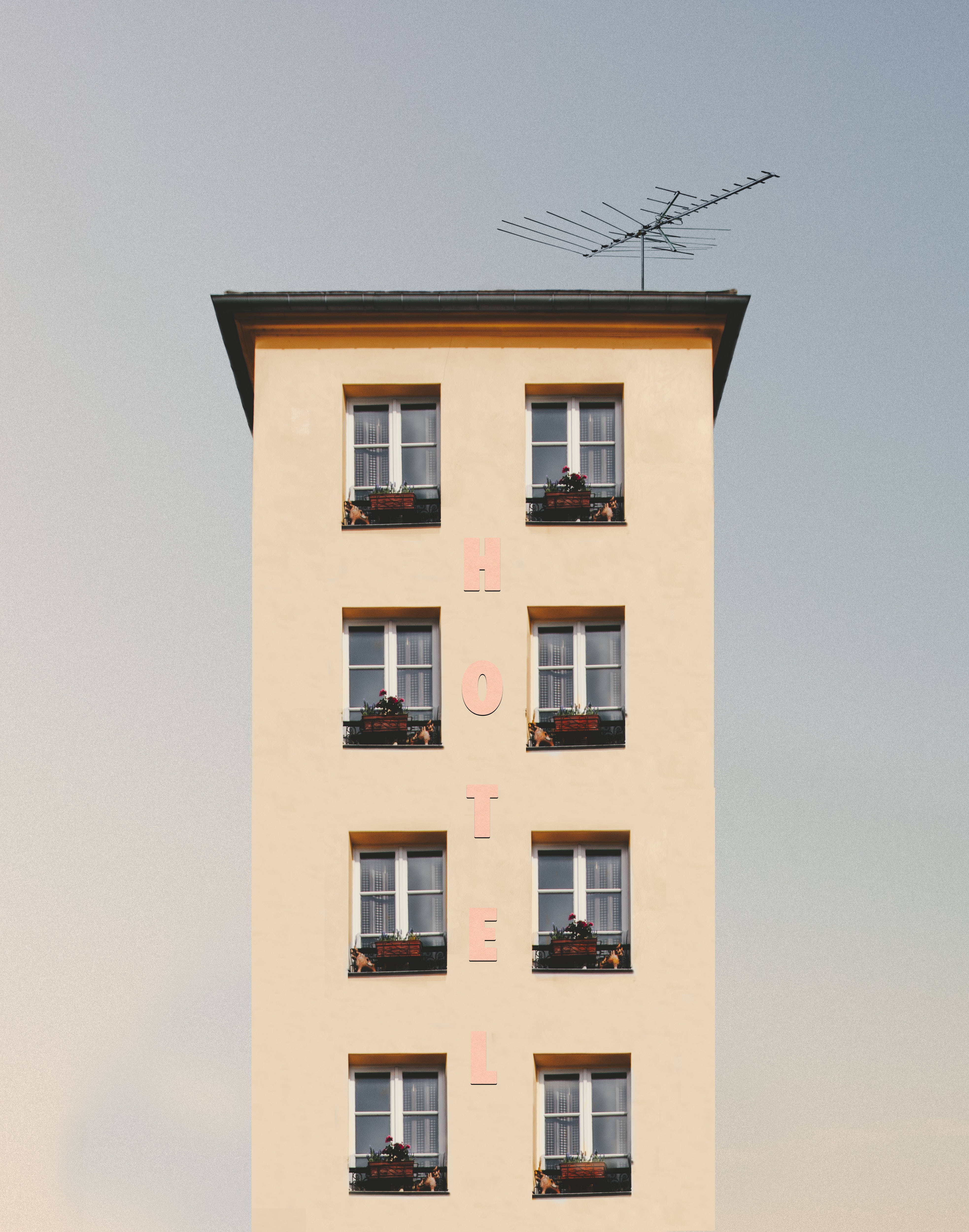 Hotel 桌布 壁紙 — 一座高大的米色飯店建築，帶有垂直的粉紅色字樣和窗台上的花箱，背景是淡色的天空。