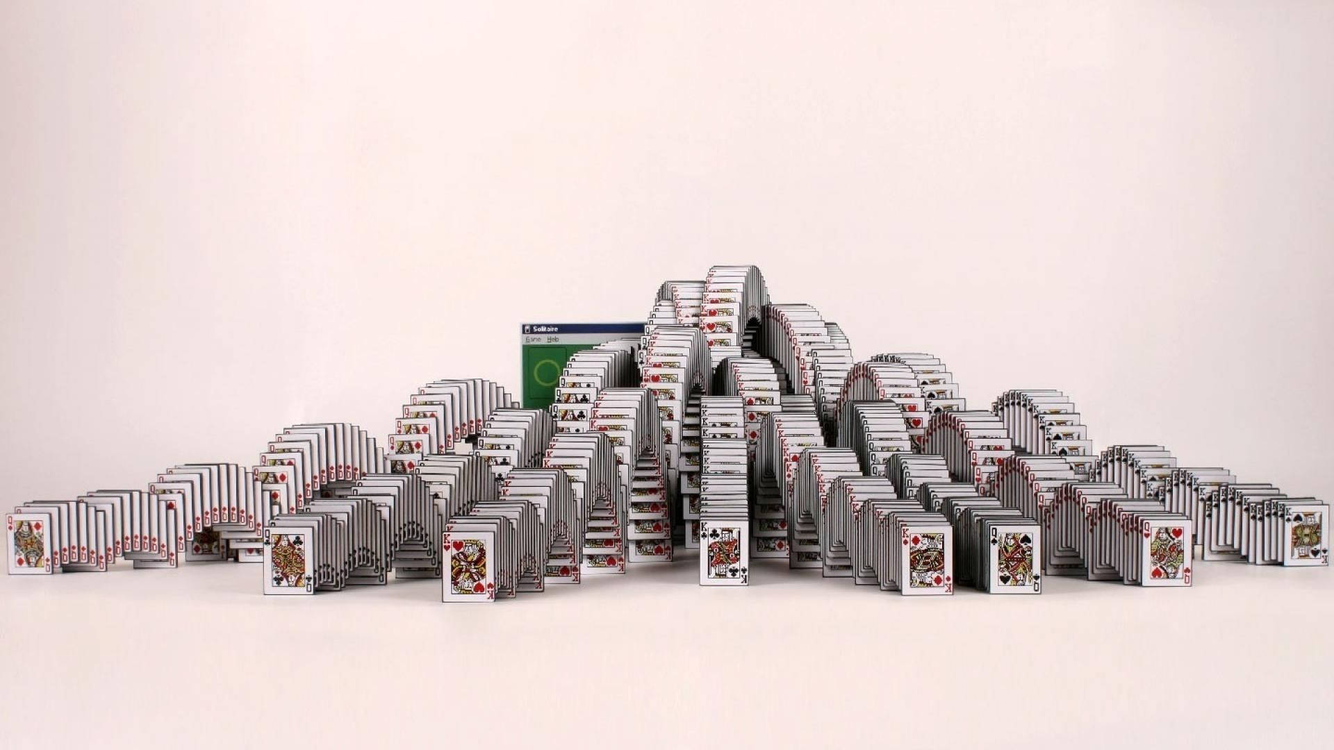 Solitaire 桌布 壁紙 — 一座高聳、複雜的雕塑，完全由撲克牌排列成對稱、層疊的行列，背景為純白色。