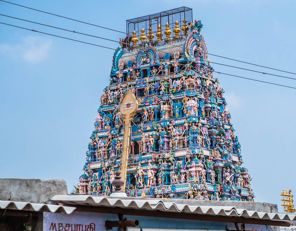 India 桌布 壁紙 — 一座高聳、雕刻精細的印度教寺廟塔門（gopuram），飾有鮮豔雕像和藍色瓷磚，在晴朗的天空下巍然聳立。