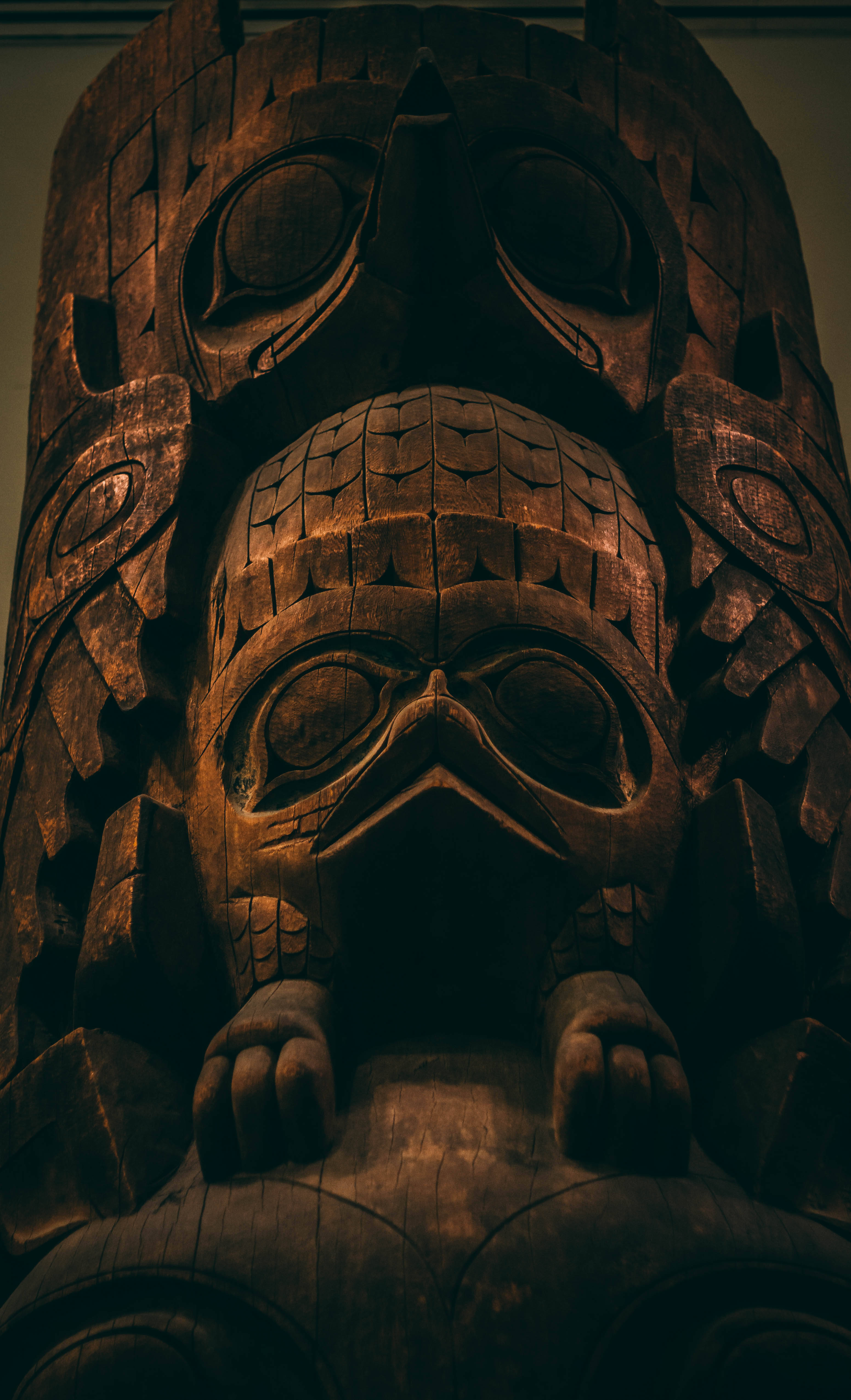 Museum 桌布 壁紙 — 一座高聳、雕刻精細的木製圖騰柱，上面有兩個堆疊的祖先面孔，被溫暖的環境光照亮。