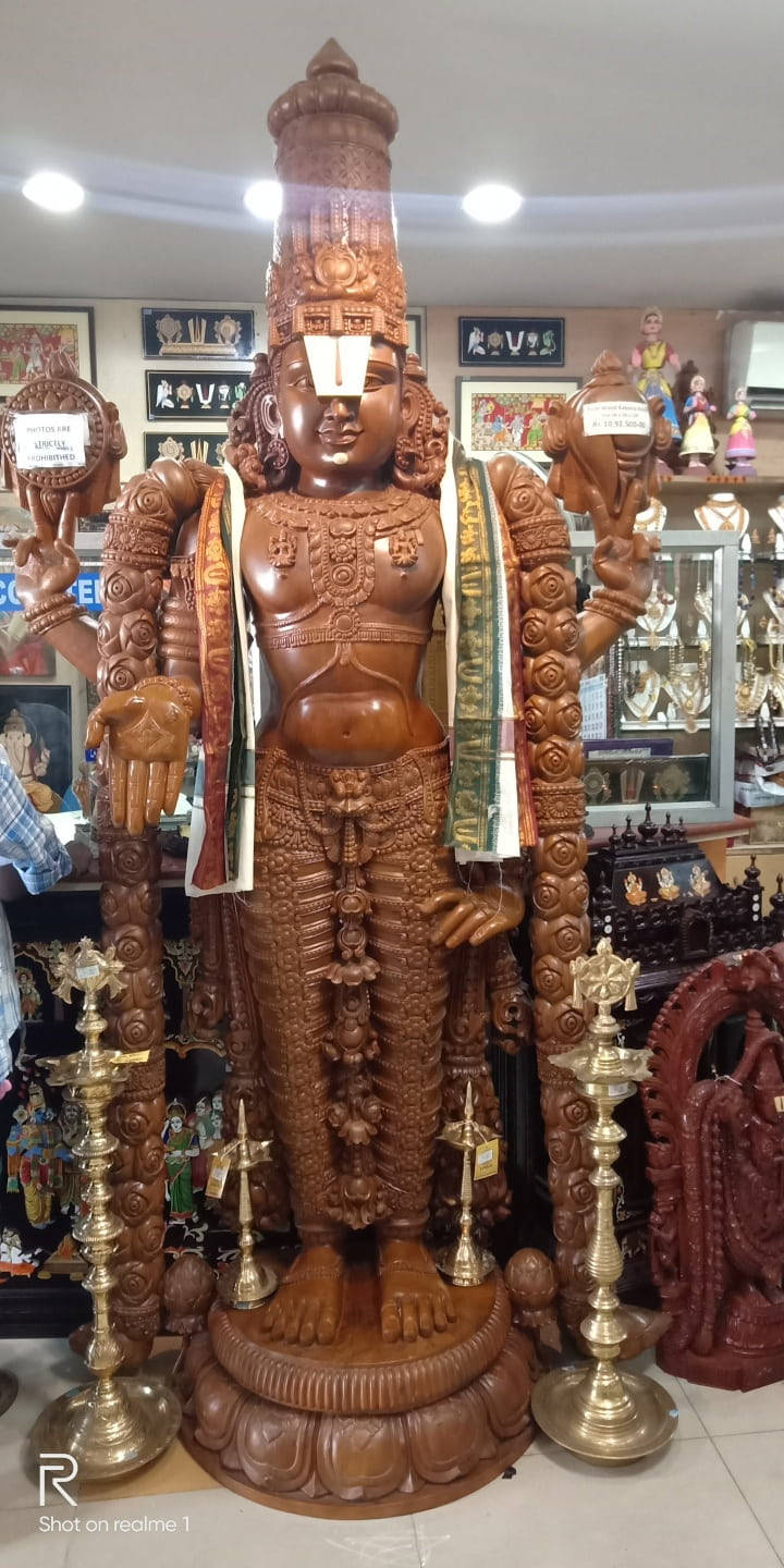 Hindi 桌布 壁紙 — 一座高聳、雕刻精緻的木製神像自豪地矗立在一間店鋪中，周圍環繞著黃銅燈具和其他宗教工藝品。